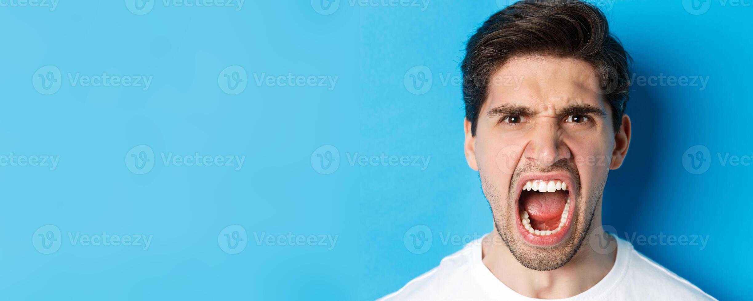 Head shot of angry man shouting and looking with hatred, standing mad against blue background photo