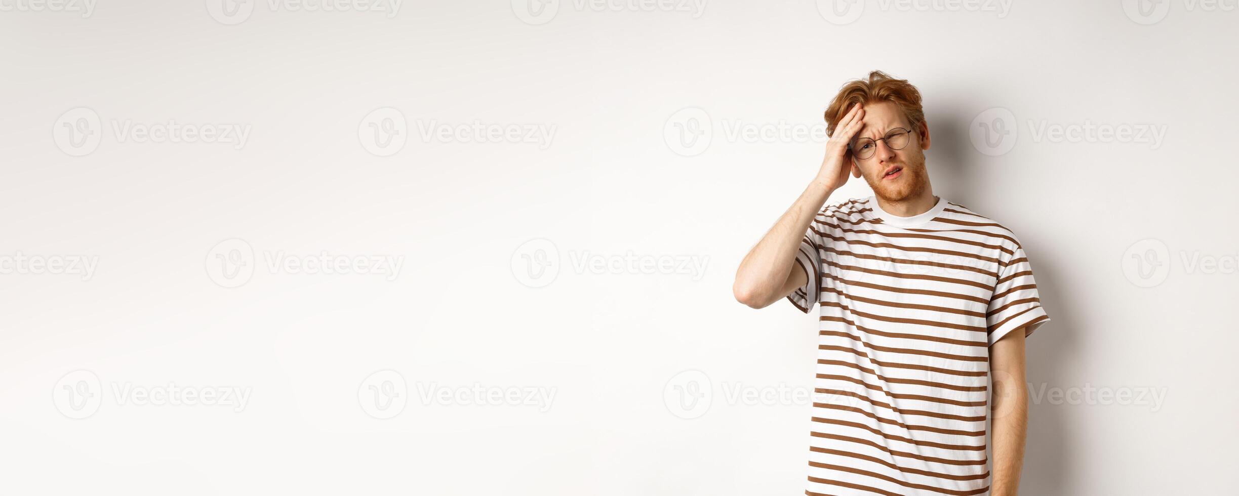 Tired young man student touching head, looking complex and tired, standing over white background photo