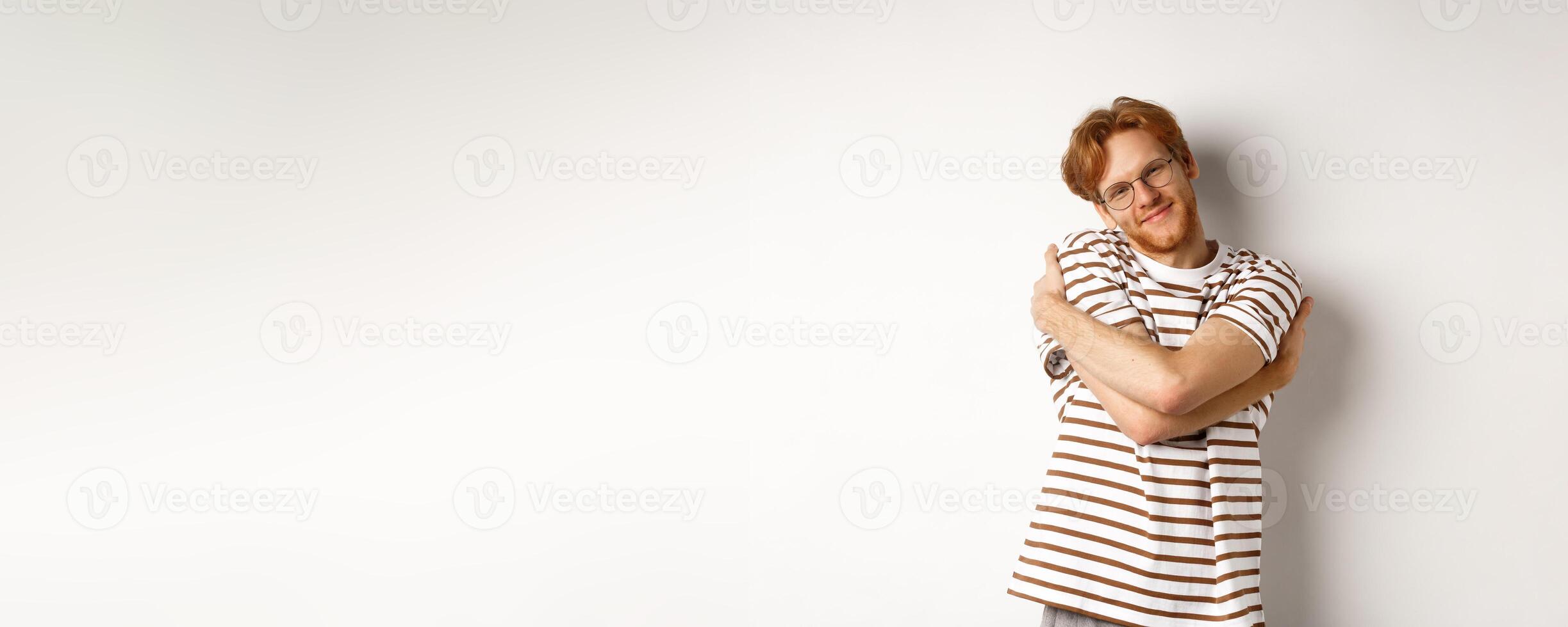 Handsome smiling man with red hair and beard looking relaxed, hugging himself and staring at camera happy face, white background photo