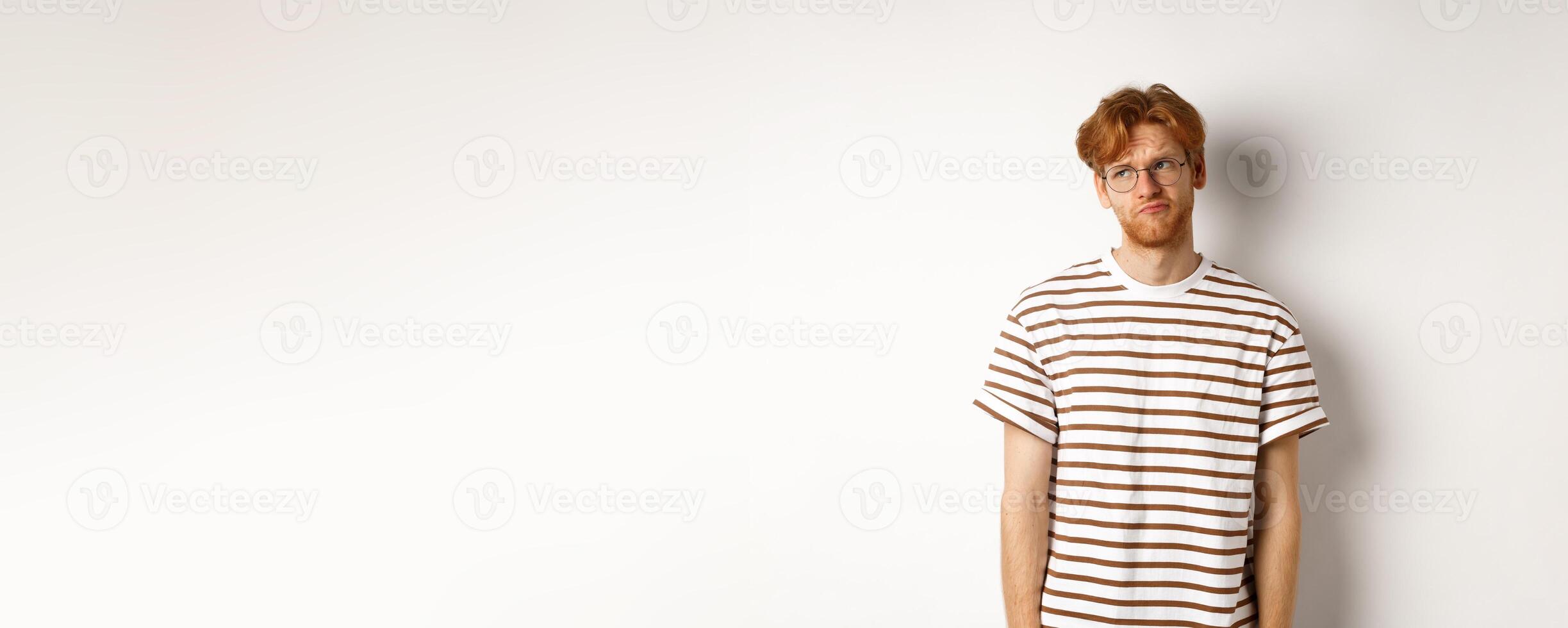 Sad and gloomy redhead man looking upper left corner, sulking and feeling like loser, standing over white background photo