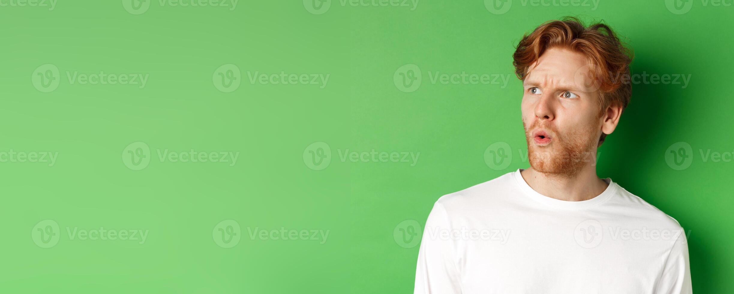 Confused redhead man staring left and looking worried, standing against green background photo