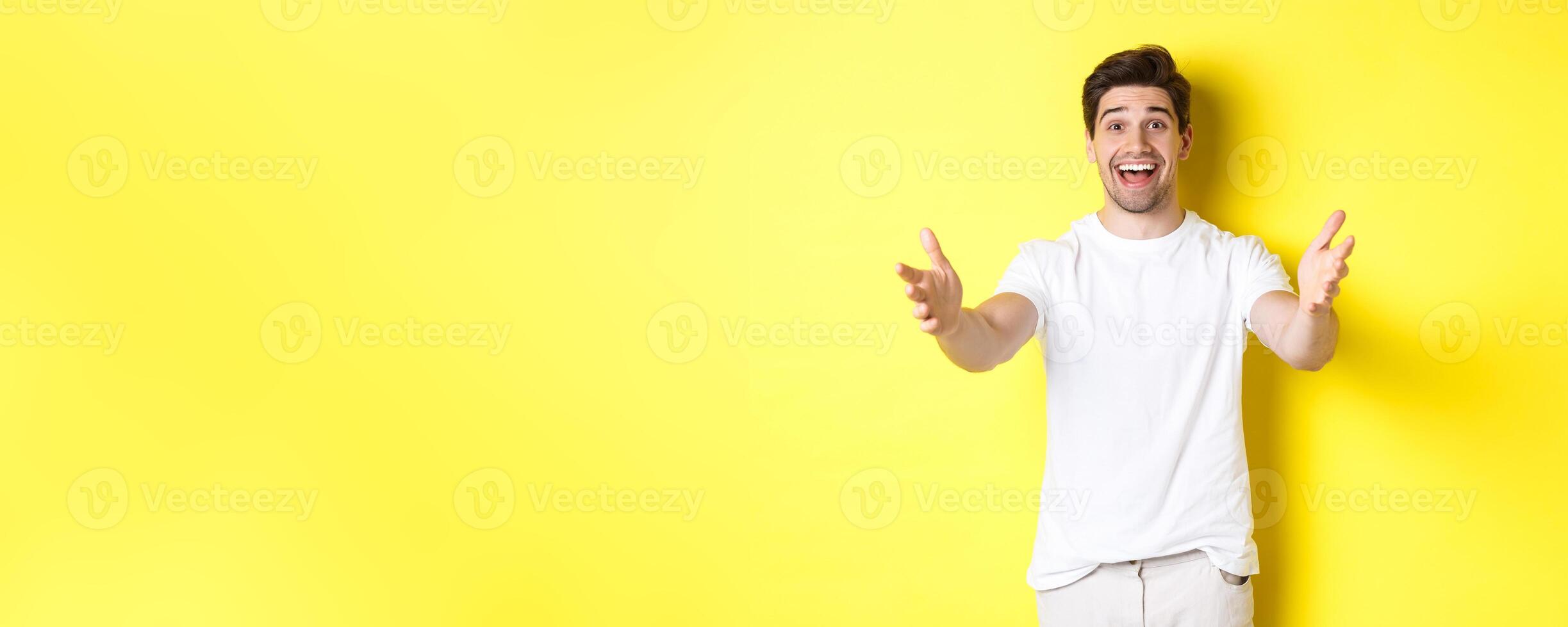 Excited handsome guy stretching hands forward, reaching for hug, receiving gift, standing over yellow background photo