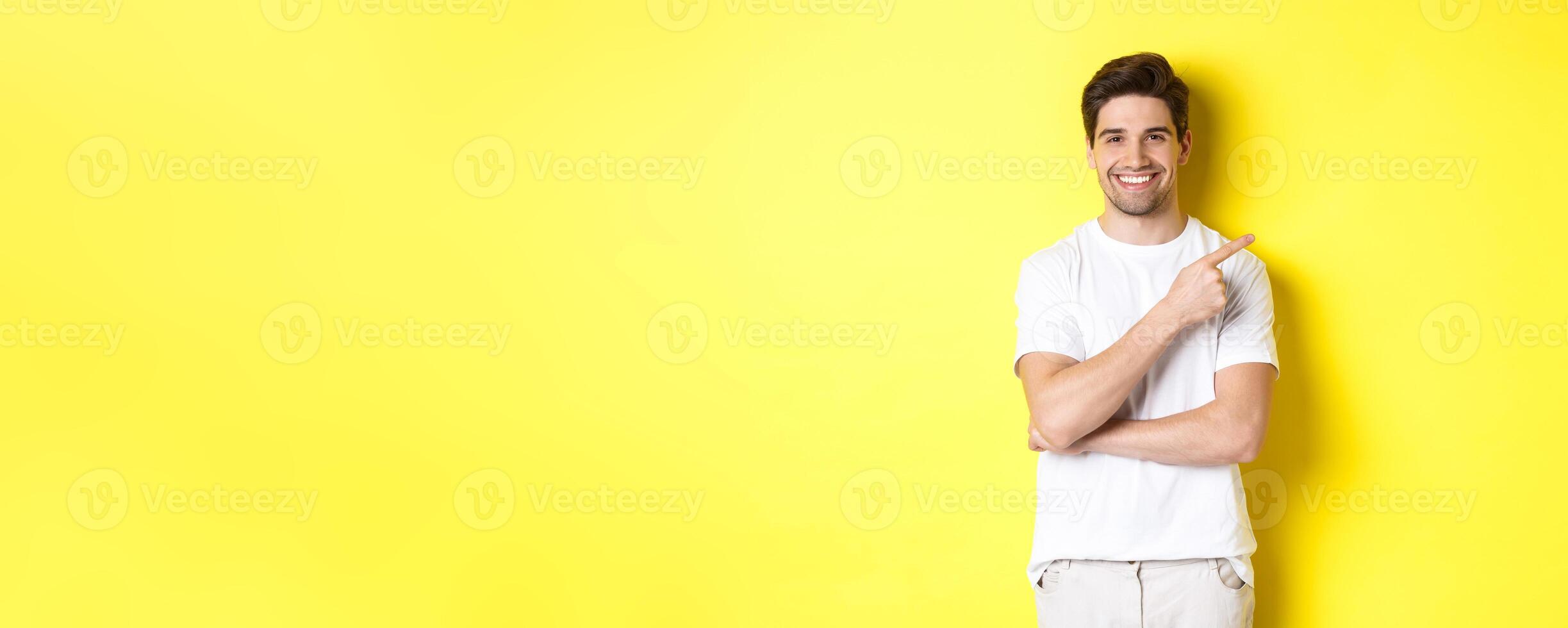 Image of attractive young man pointing finger right at copy space, showing banner or promo offer, standing over yellow background photo