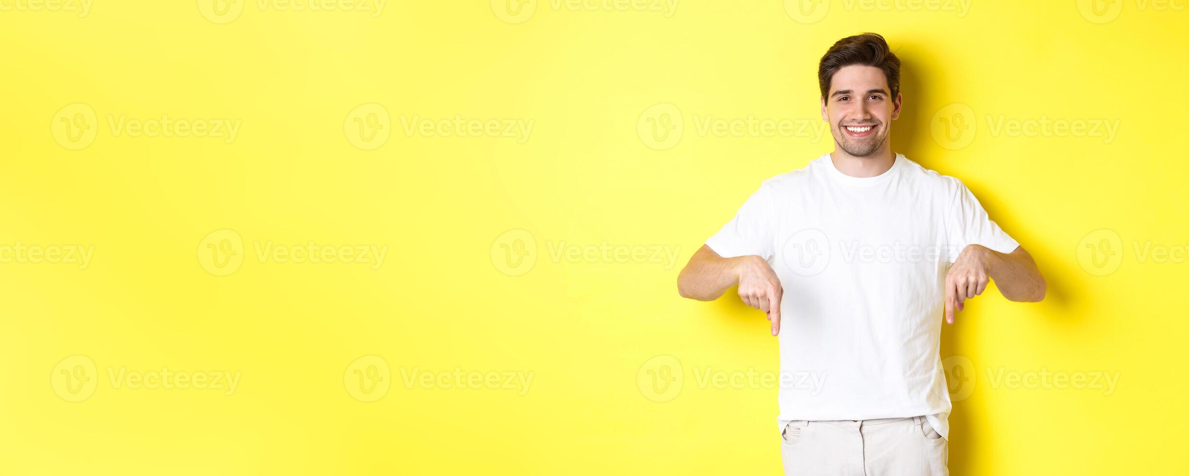 Attractive bearded man pointing fingers down, showing event banner, standing over yellow background photo