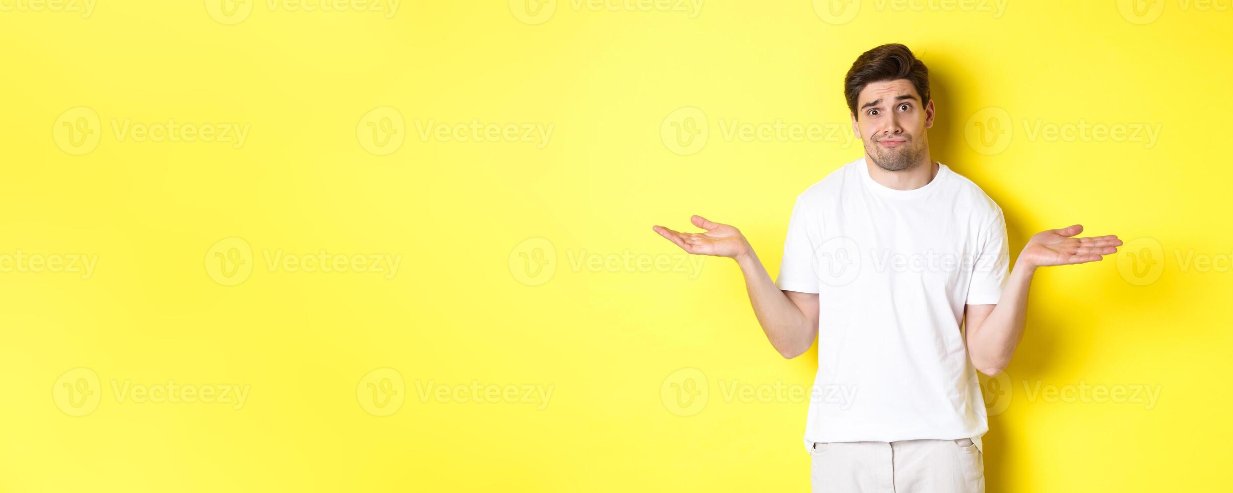 Clueless man in white t-shirt, shrugging and looking puzzled, dont know anything, standing over yellow background photo