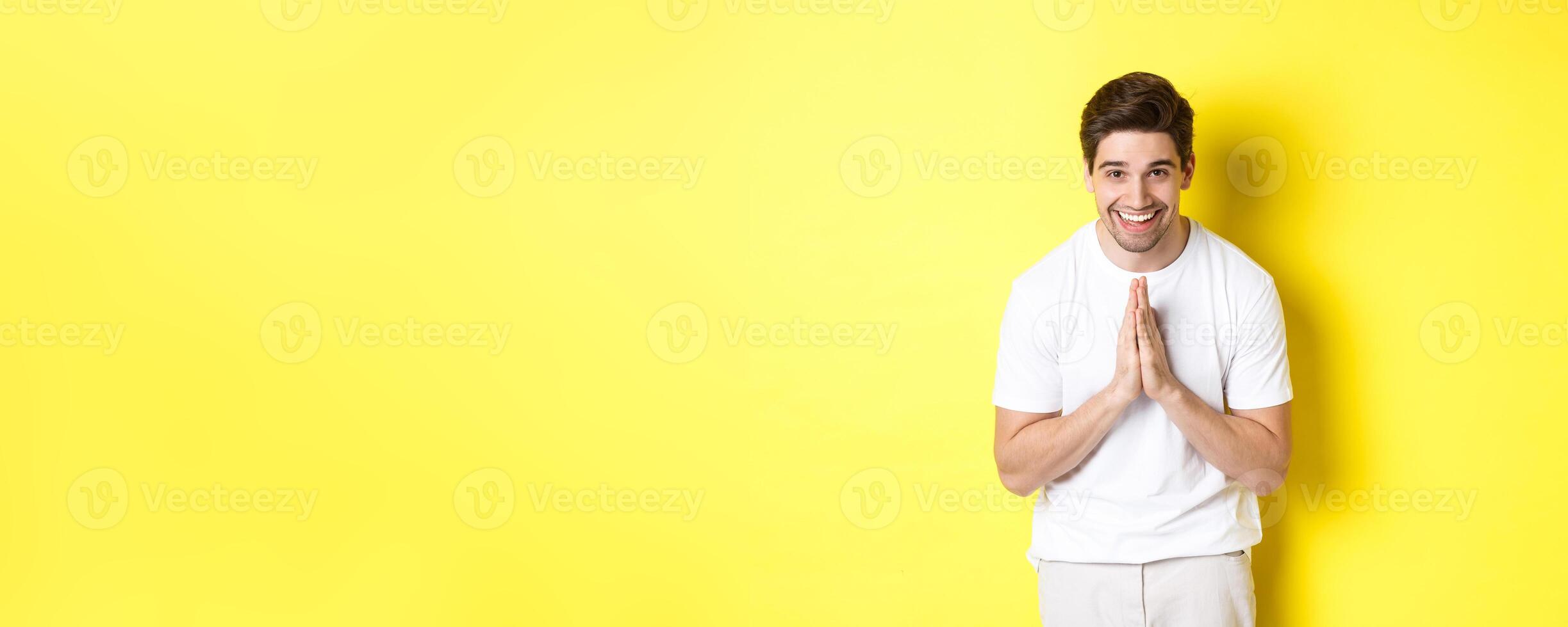 Handsome guy saying thank you, bowing and holding hands in namaste gesture, express gratitude, standing over yellow background photo