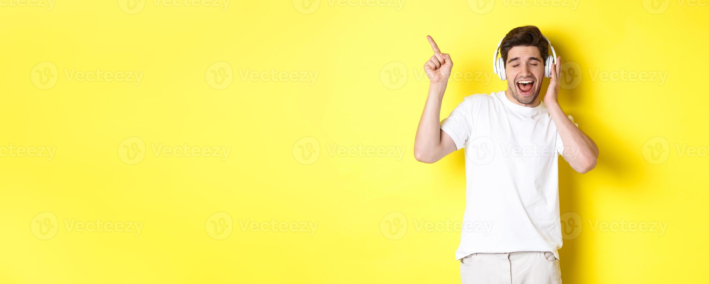 Happy man listening music in headphones, pointing finger at promo offer for black friday, standing over yellow background photo