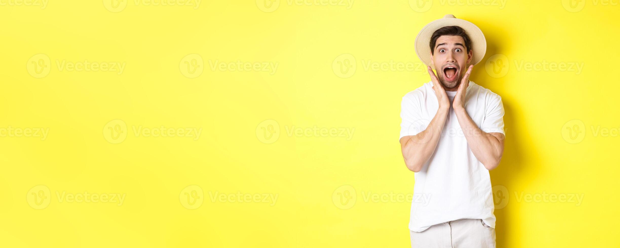 Concept of tourism and summer. Surprised male model in straw hat, looking amazed at special offer, standing against yellow background photo