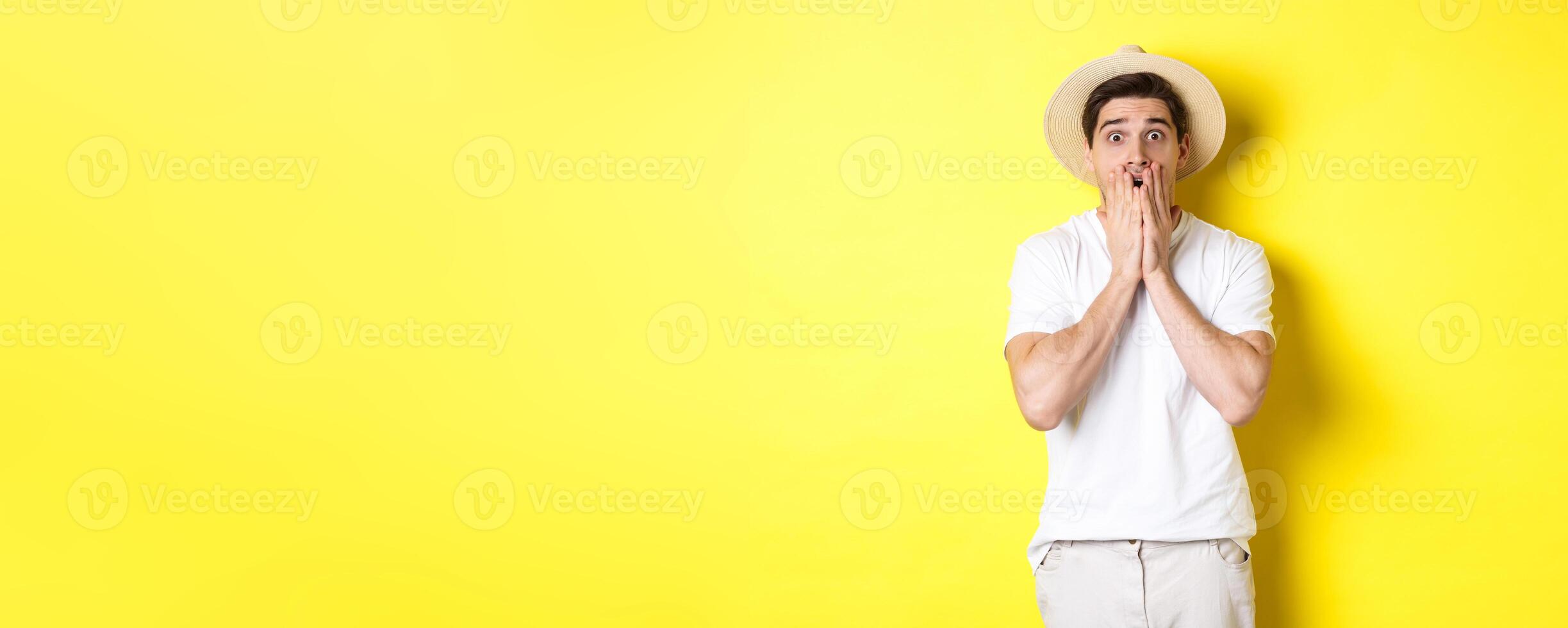 Concept of tourism and summer. Shocked guy jumping from fear, standing startled against yellow background photo