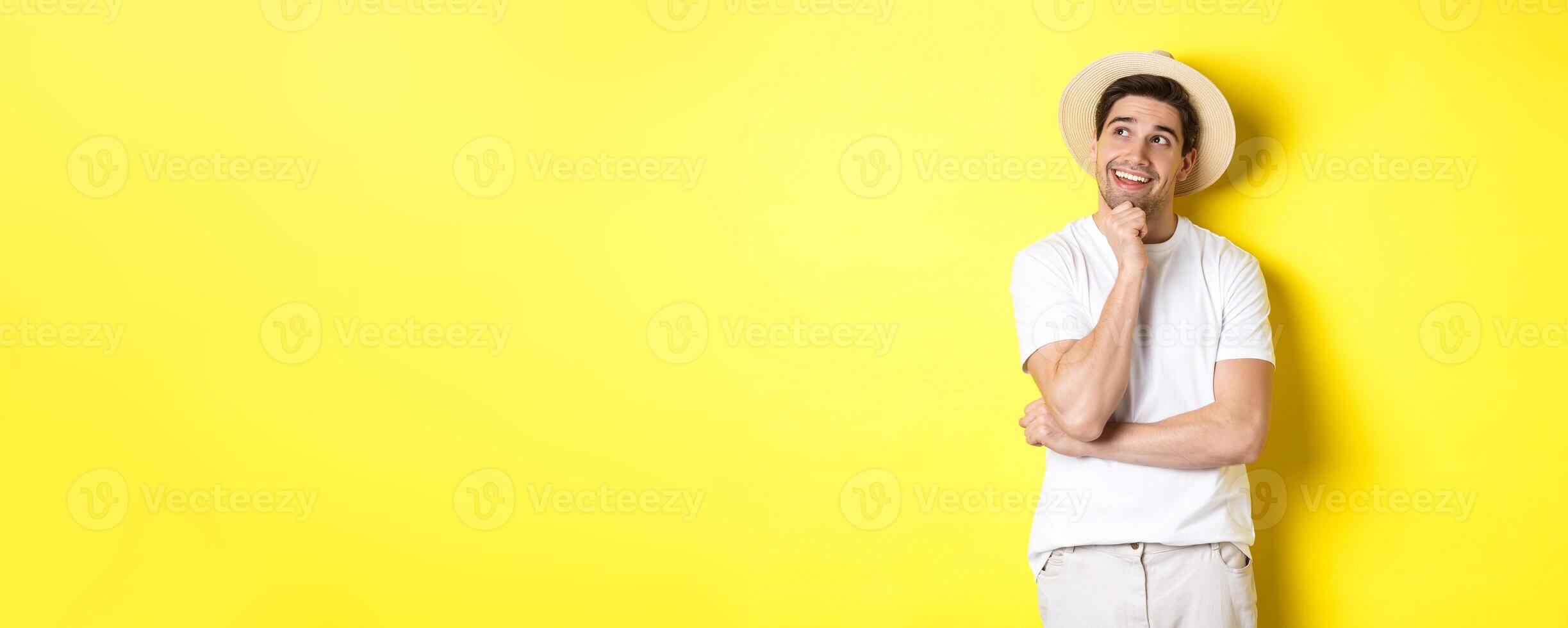 Young thoughtful man tourist imaging something, looking at upper left corner and smiling, thinking and standing over yellow background photo