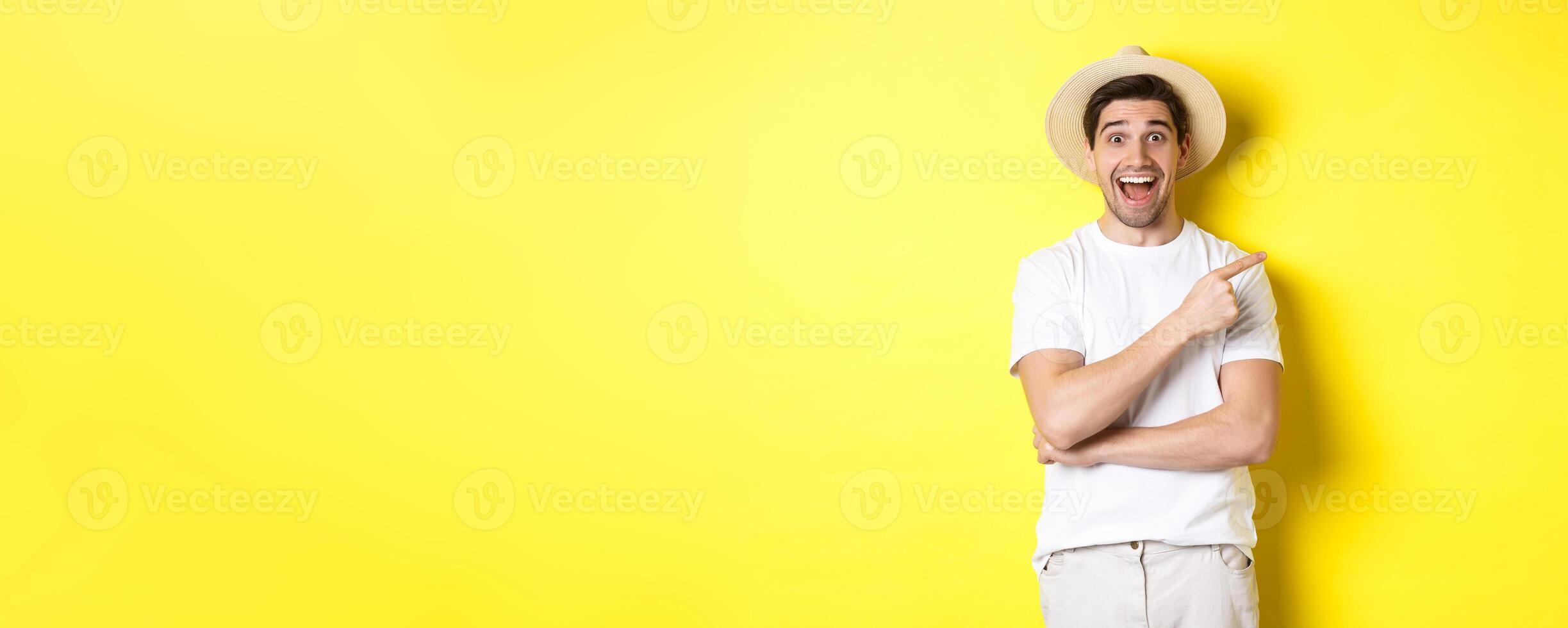 Happy male tourist in straw hat pointing finger right, showing promo offer on copy space, yellow background photo