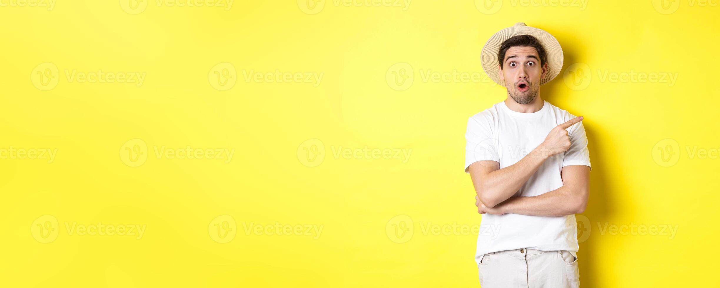 Surprised man in straw hat pointing finger right, showing promo banner, standing over yellow background photo