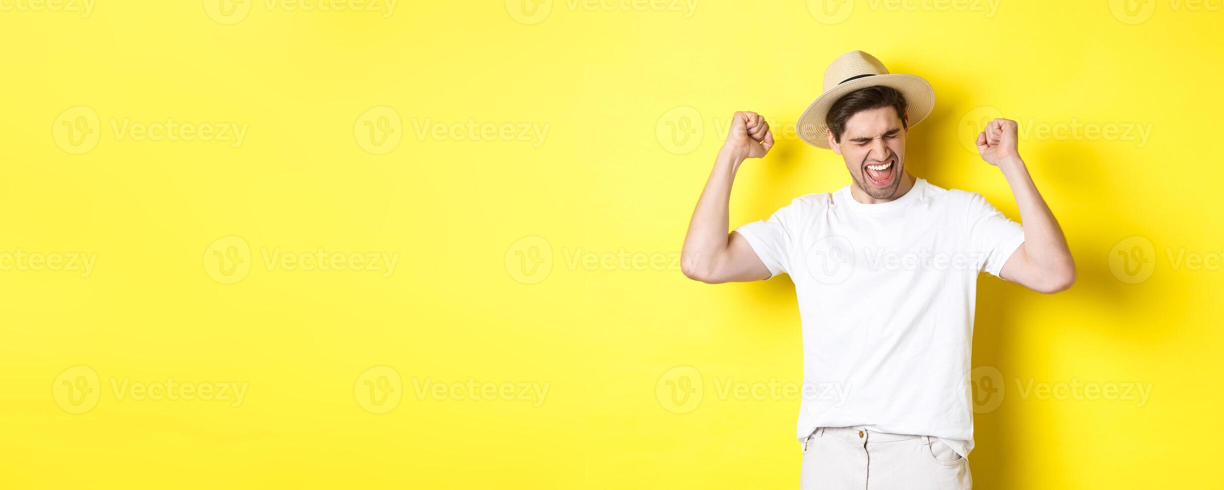 Concept of tourism and vacation. Happy man rejoicing, winning something or achieve goal, triumphing against yellow background photo