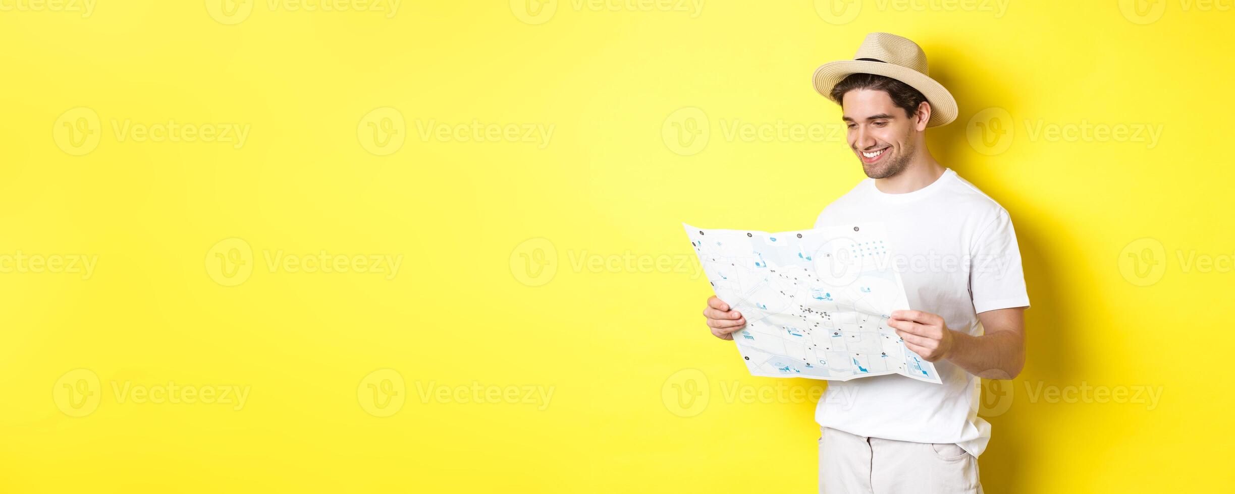 Travelling, vacation and tourism concept. Smiling happy tourist looking at map with sightseeings, standing against yellow background photo