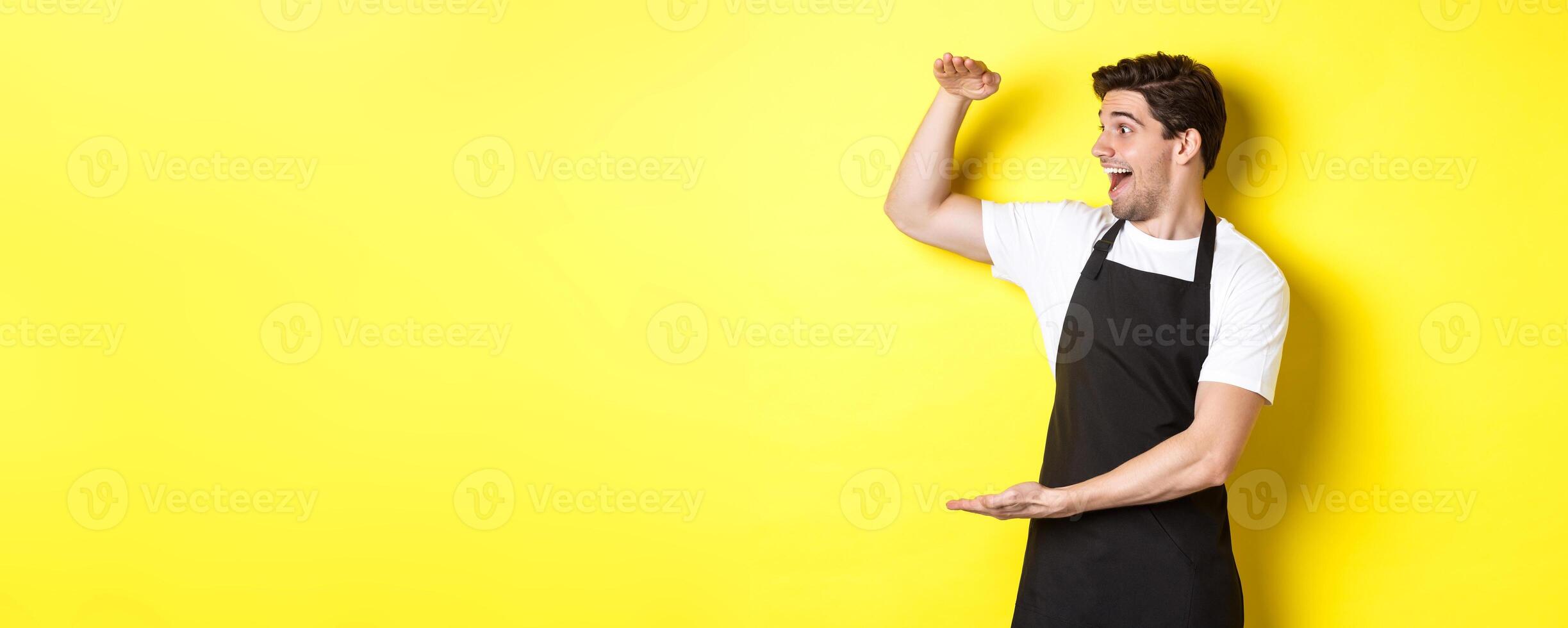Man looking surprised at something large, standing in black apron against yellow background photo