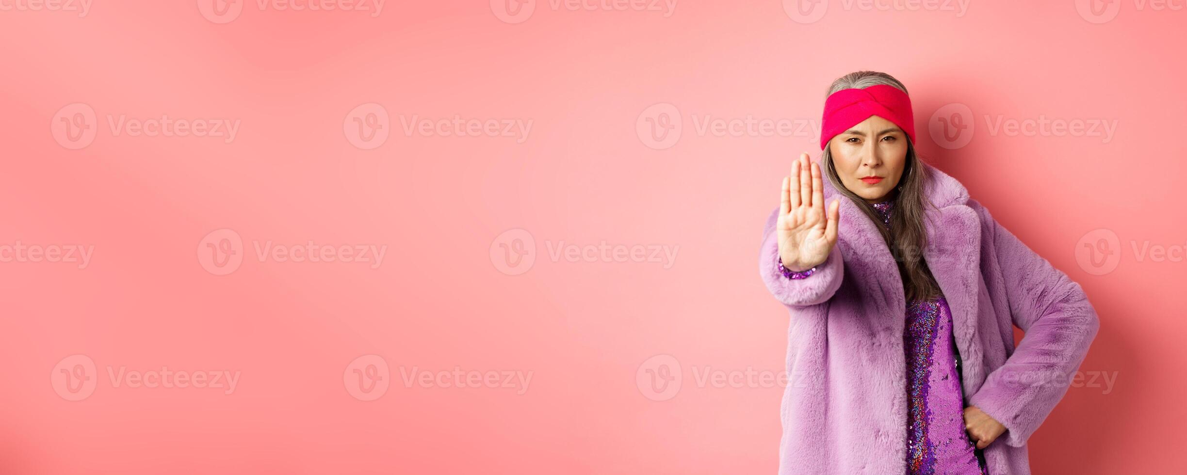 Fashion and shopping concept. Serious asian senior woman showing stop sign to warn and prohibit something, looking determined at camera, wearing stylish purple clothes photo