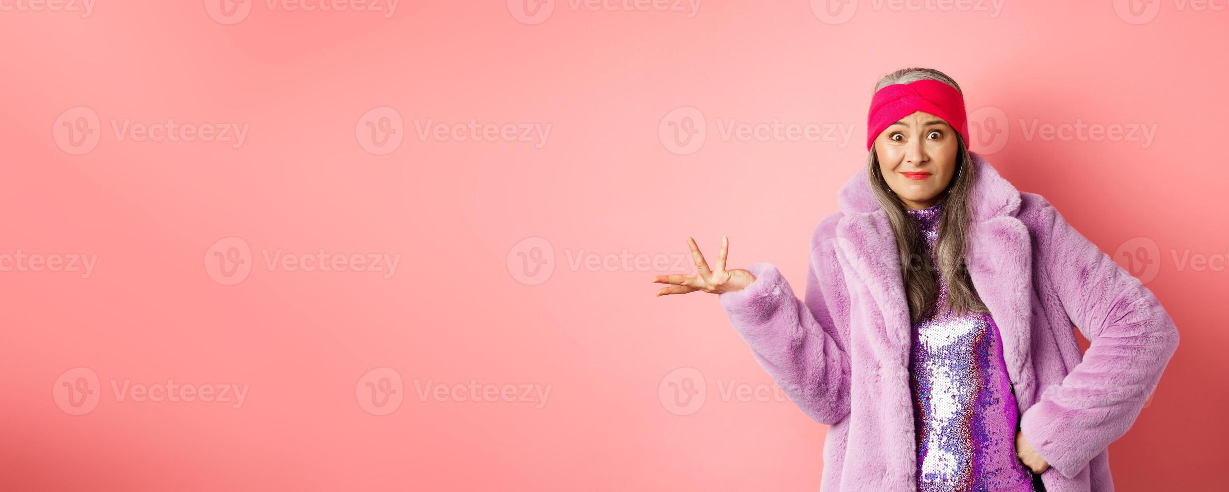 Fashion and shopping concept. Confused senior hipster woman looking puzzled, shrugging with hand spread sideways and clueless stare, standing over pink background photo