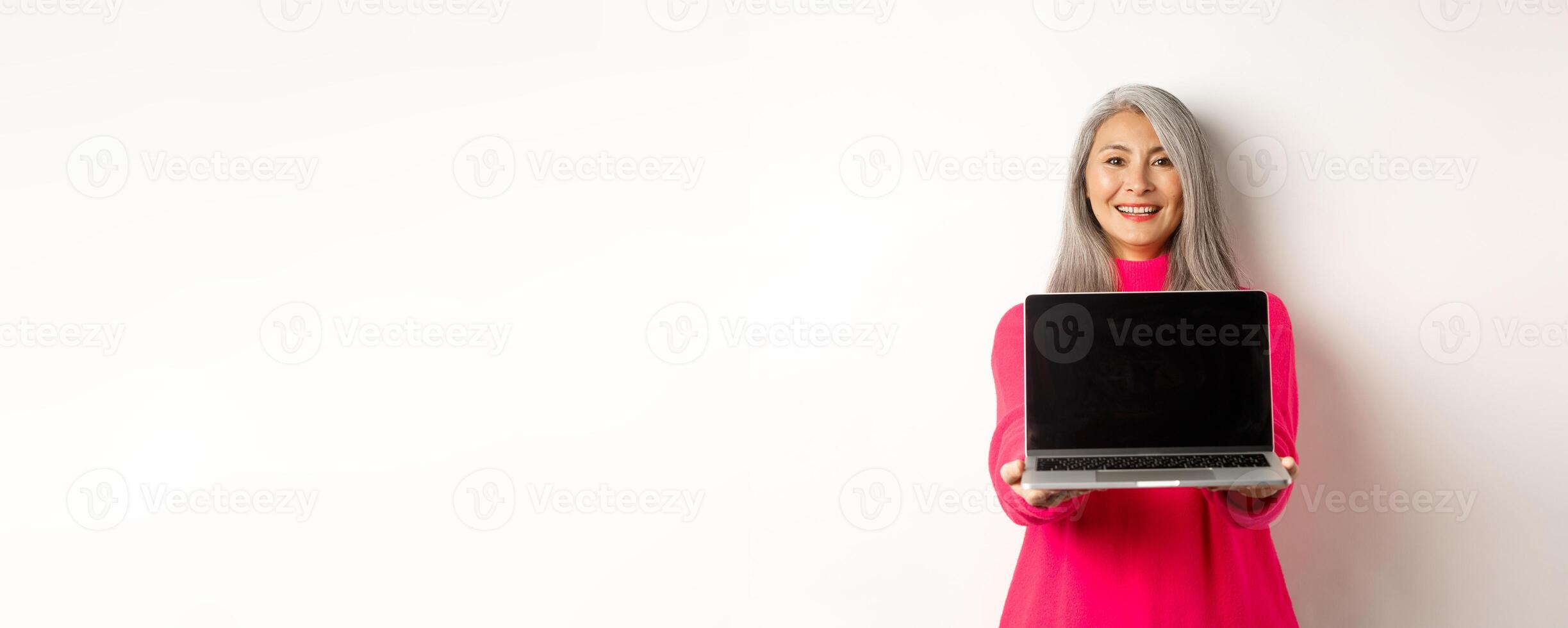 E-commerce concept. Smiling asian senior woman showing blank laptop screen and looking happy, demonstrating promo, white background photo