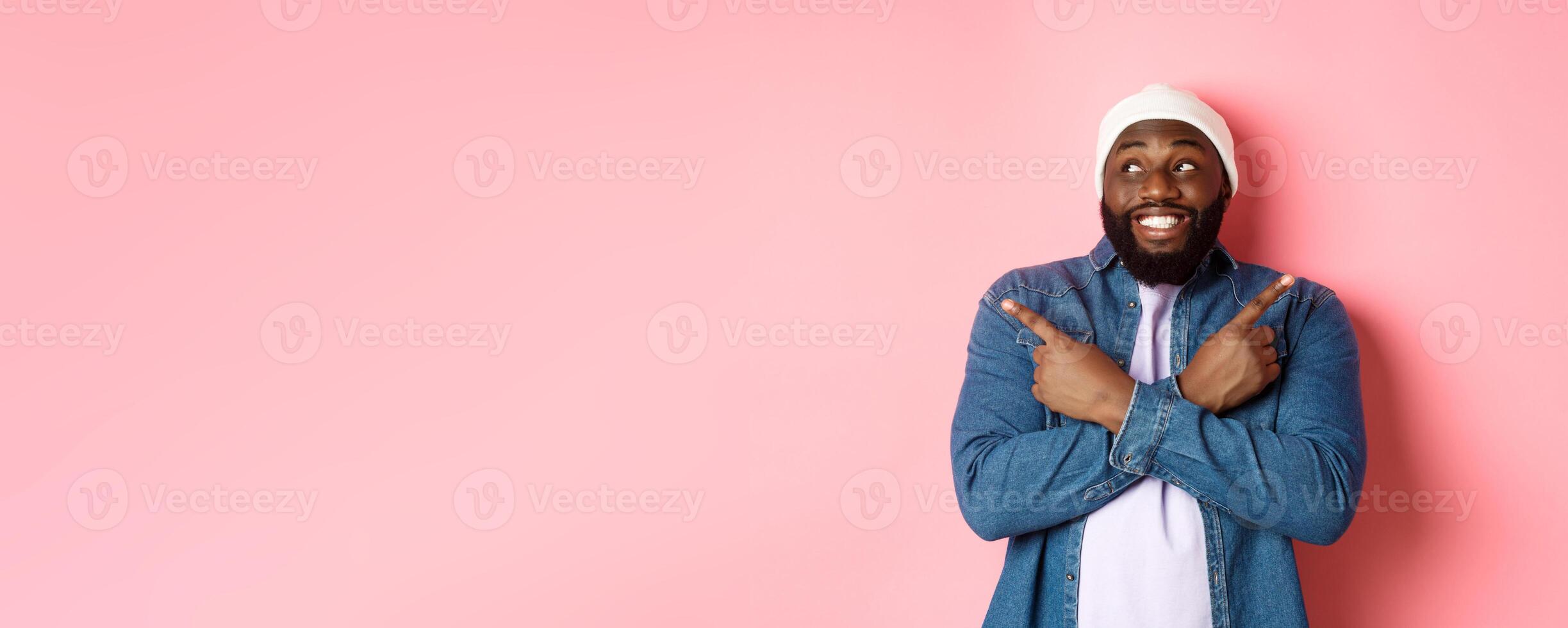 Excited young african-american man pointing sideways, showing two choices and making decision, smiling happy, standing over pink background photo