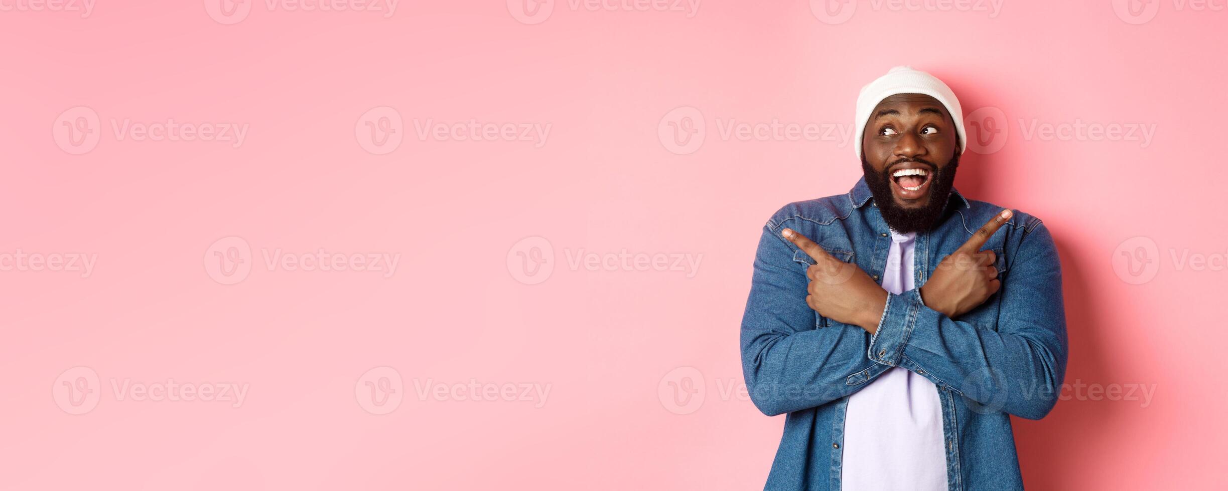 Excited young african-american man pointing sideways, showing two choices and making decision, smiling happy, standing over pink background photo