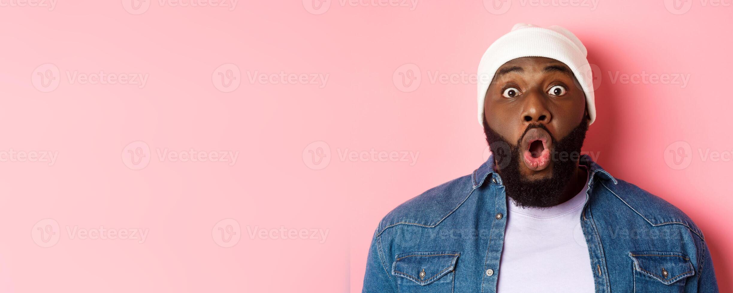 Close-up of impressed Black male model saying wow, staring at camera amazed and wondered, standing over pink background photo