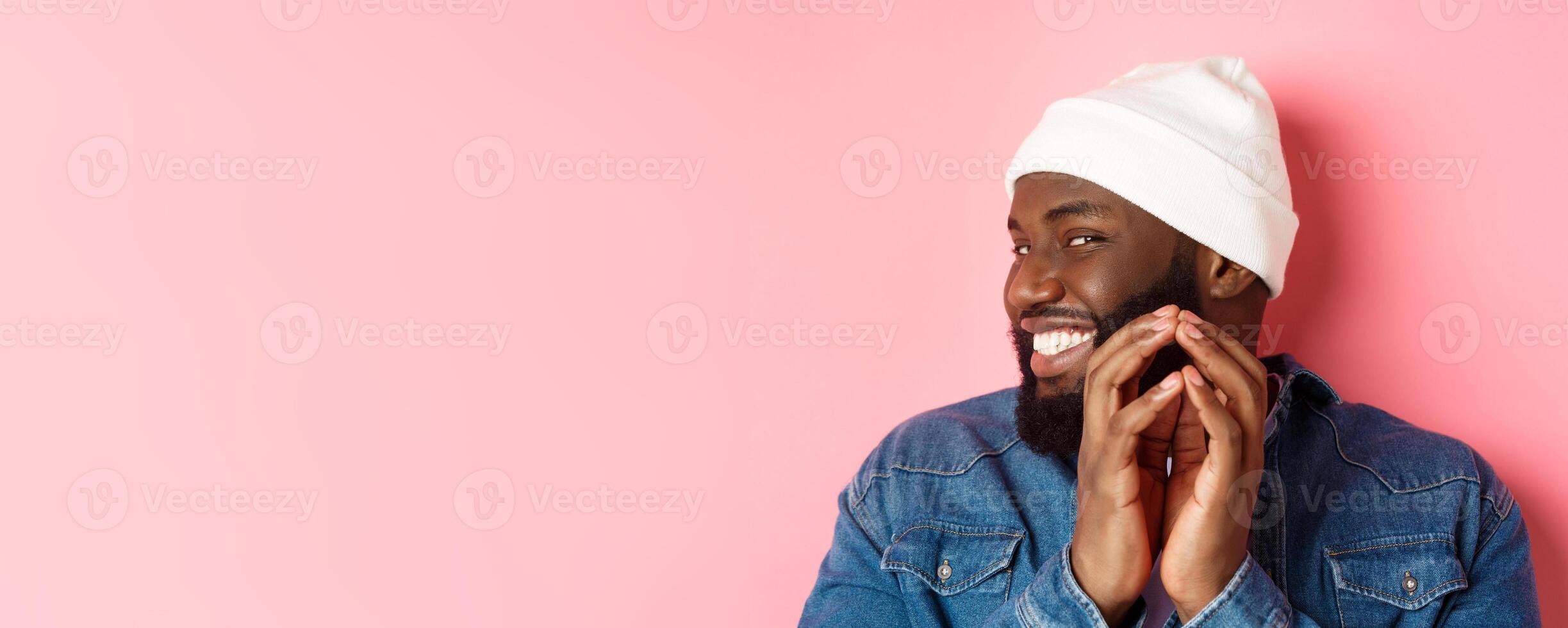 Close-up of devious african-american male model having an idea, scheming something, steeple fingers and smiling sly, standing over pink background photo