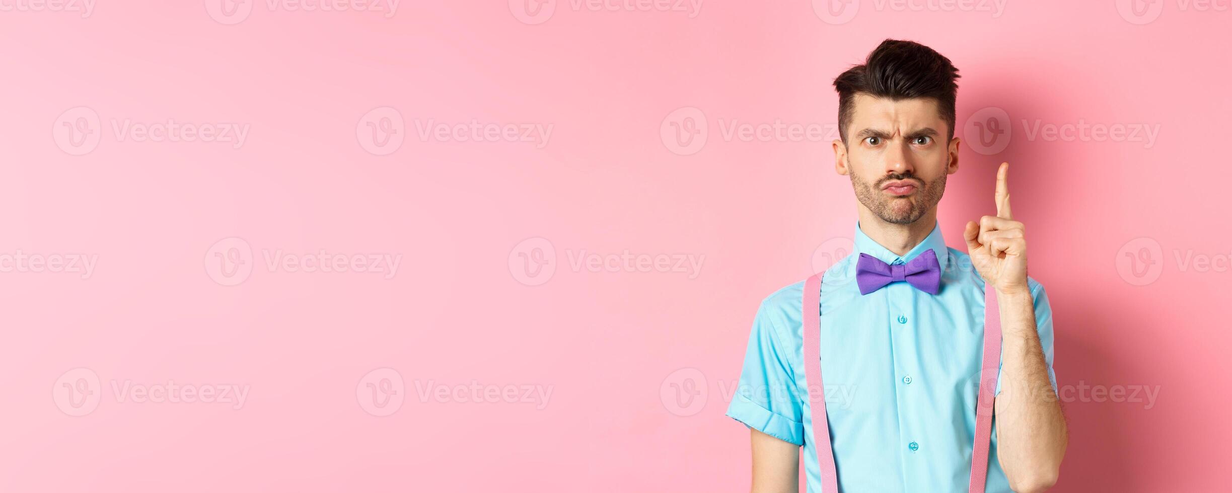 Angry male teacher shaking finger and scolding someone who misbehave, frowning grumpy, and teaching lesson, standing over pink background photo