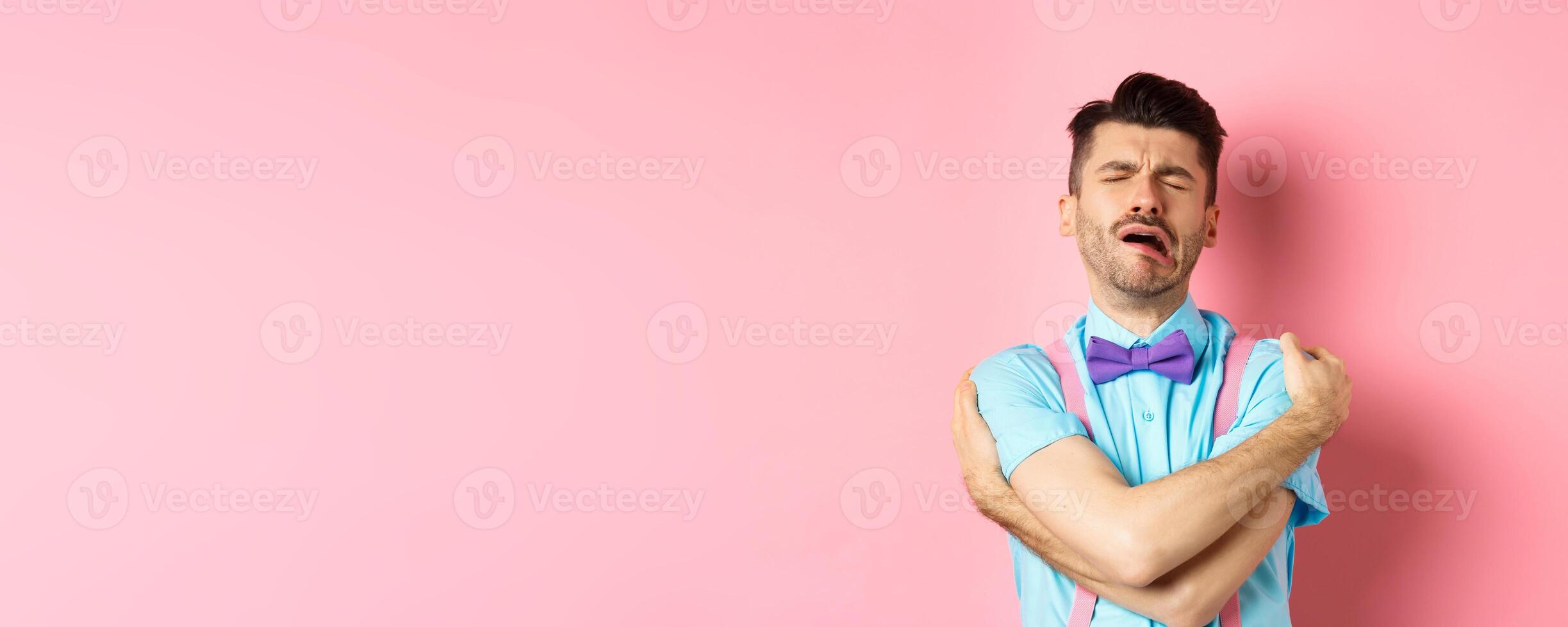 Crying guy hugging himself, feeling sad and lonely, standing unhappy on pink background photo