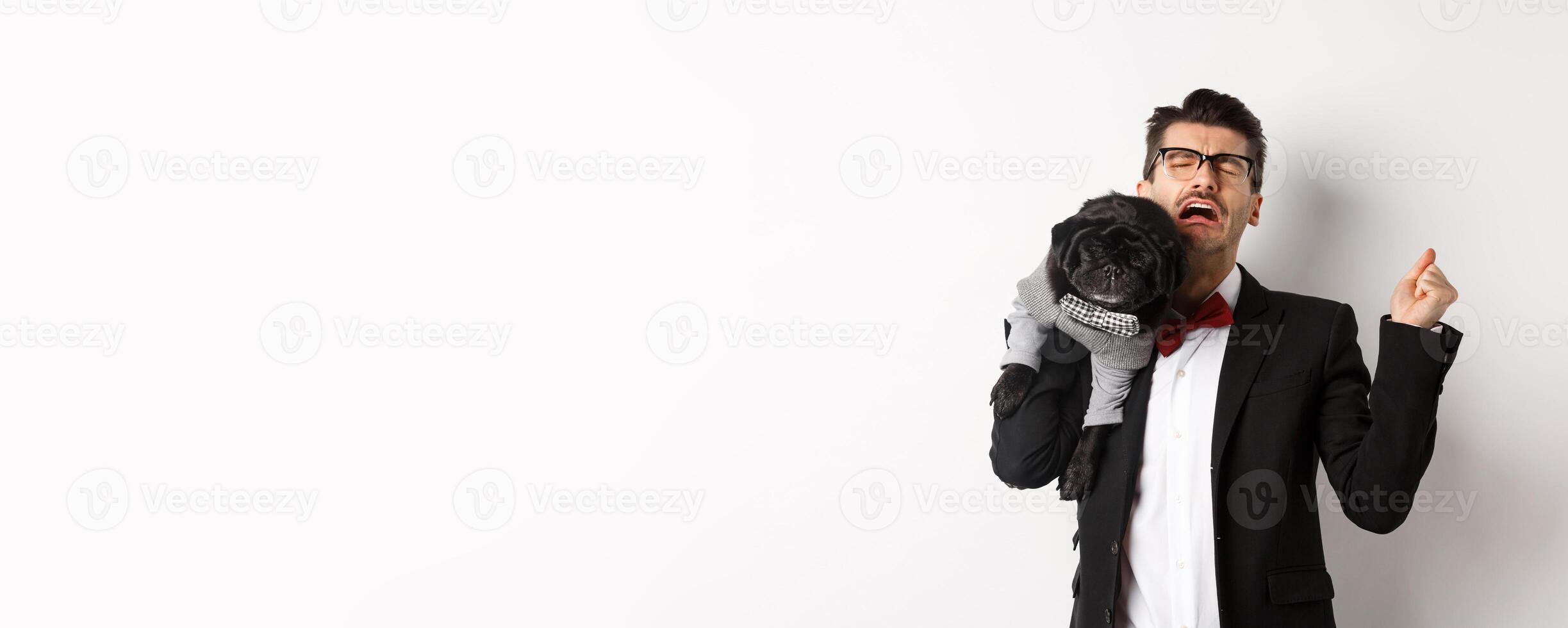 Sad man in suit, holding cute small dog on shoulder and crying with disappointed face, standing distressed over white background photo