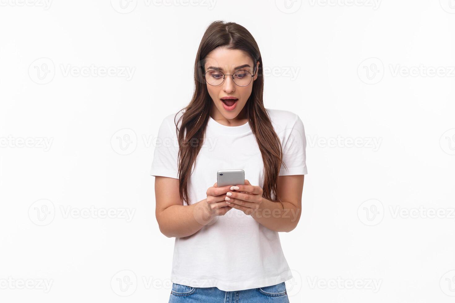 Communication, technology and lifestyle concept. Portrait of surprised and amazed, excited young caucasian woman in glasses, looking at mobile phone, receive awesome new via text message photo