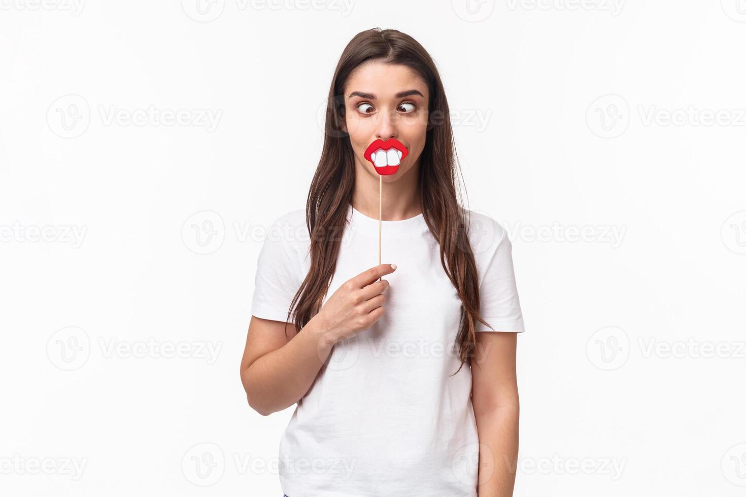 Entertainment, fun and holidays concept. Portrait of funny and joyful celebrating fools day april first, having fun, holding stick with lips and big teeth, show hilarious grimaces, white background photo