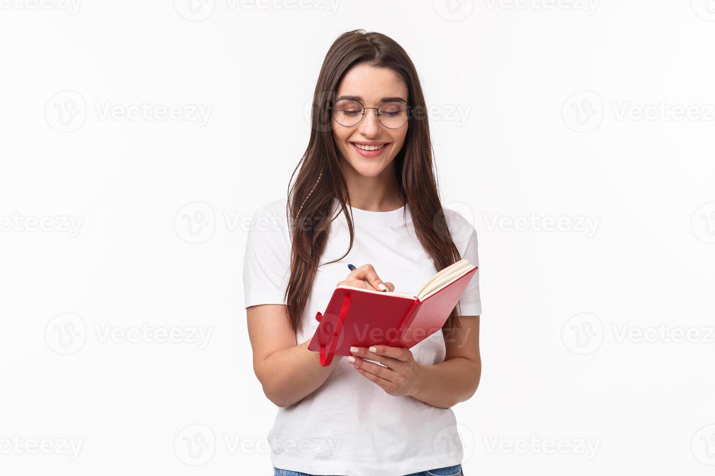 Portrait of smiling pretty caucasian girl writing in her diary, prepare homework for english courses, smiling, have inspiration to write plans for next week in planner, white background photo