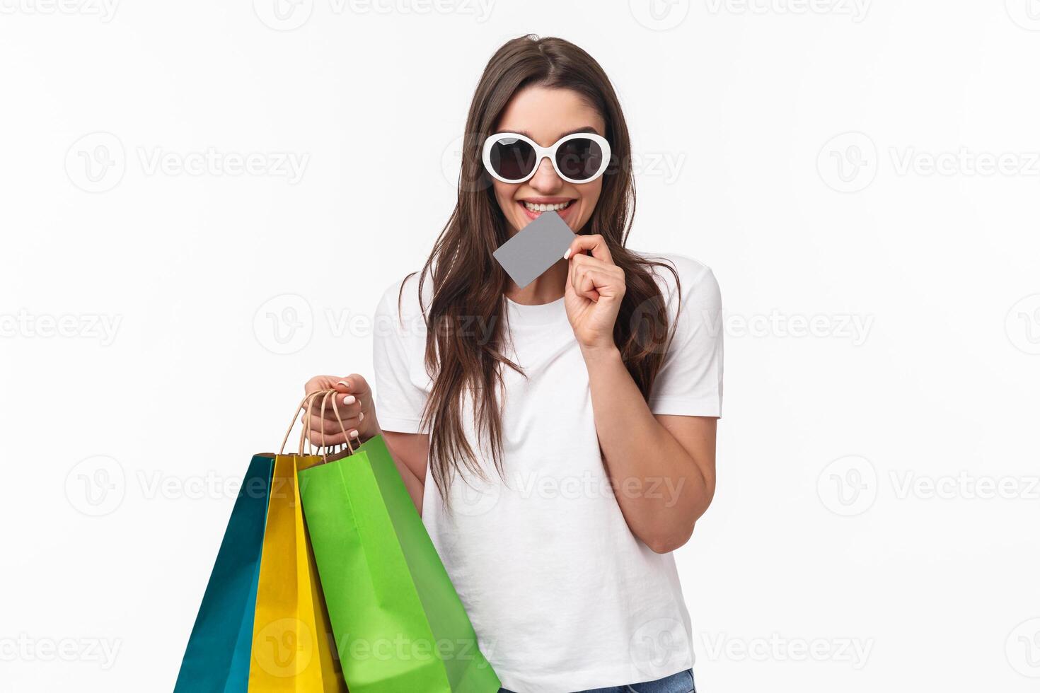 Shopping, leisure and lifestyle concept. Portrait of excited beautiful young woman cant wait to waste all her money, biting credit card and look thrilled, think what store visit next, hold shop bags photo