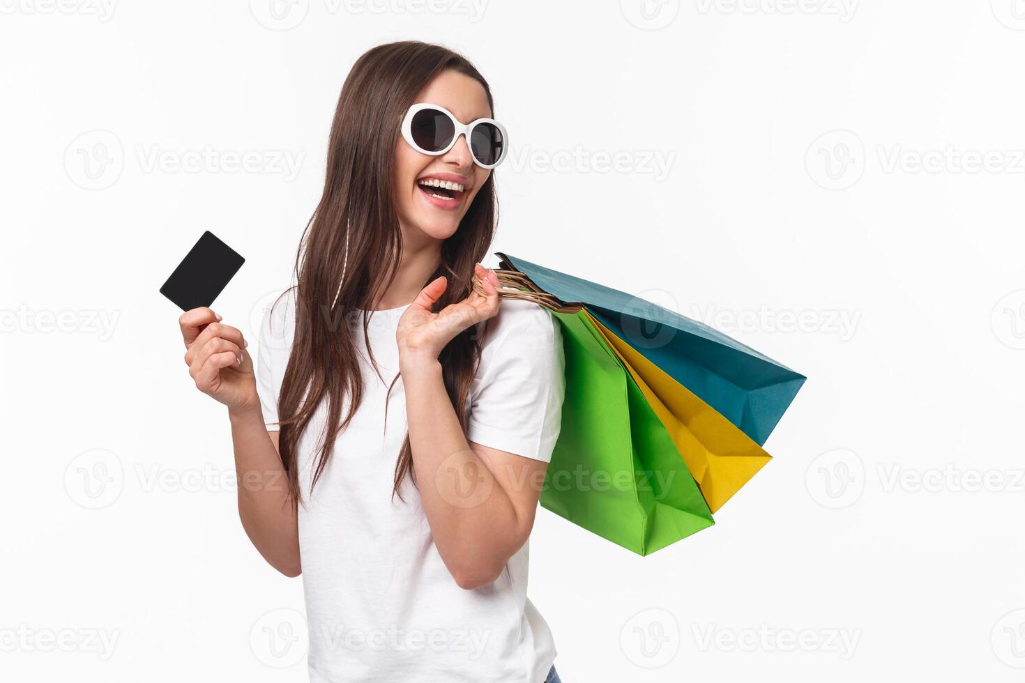 Shopping, leisure and lifestyle concept. Portrait of carefree happy young woman release stress with buying new things, paying with credit card, hold shop bags on shoulder and looking back smiling photo