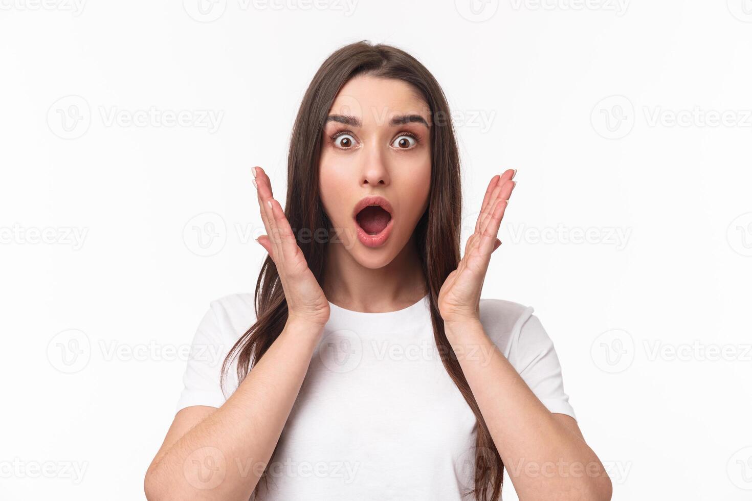 What an amazing news. Surprised and astonished, excited young woman react to something awesome happened, gasping, open mouth and raise hands near face, staring camera, white background photo