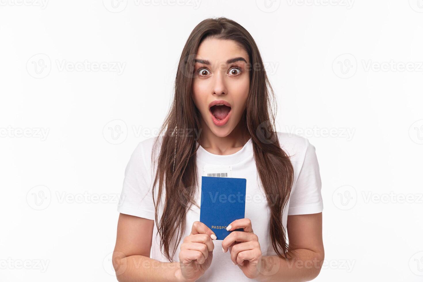 Travelling, holidays, summer concept. Close-up portrait of impressed, shocked young woman holding passport, drop jaw and staring astonished at camera, ready to travel, moving abroad photo