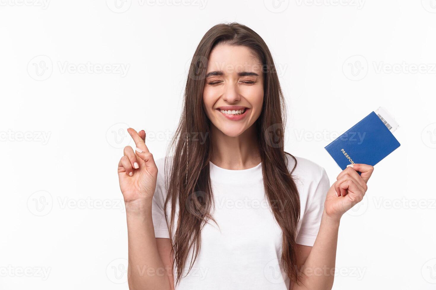 Travelling, holidays, summer concept. Journey beggings. Happy cheerful brunette girl in t-shirt, close eyes and smiling, making wish, cross fingers good luck, holding passport with plane ticket photo