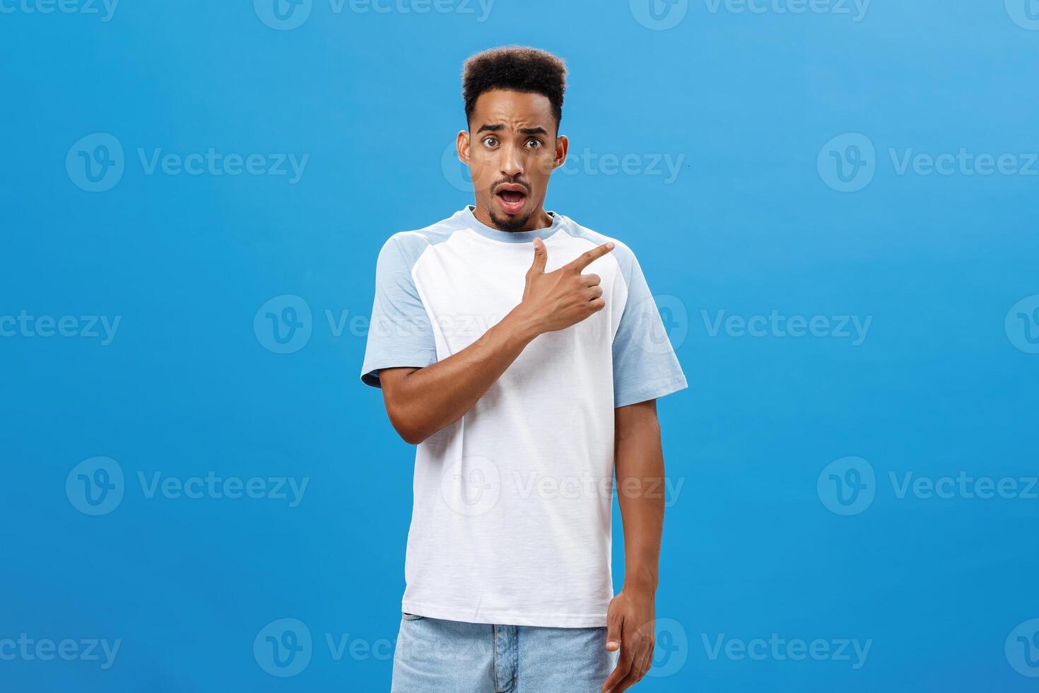 Man feeling shocked finding out friend betrayed him pointing at upper right corner frowning and opening mouth with concerned upset and unhappy expression posing over blue background worried photo