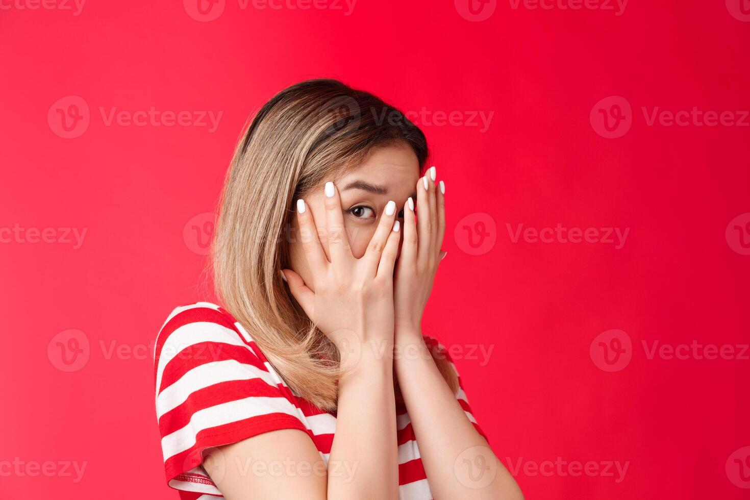 Not looking swear. Cute peeking young girl close eyes palms turn away stare one eye camera curiously, wanna see what happening, dying interest know what happening, stand red background photo