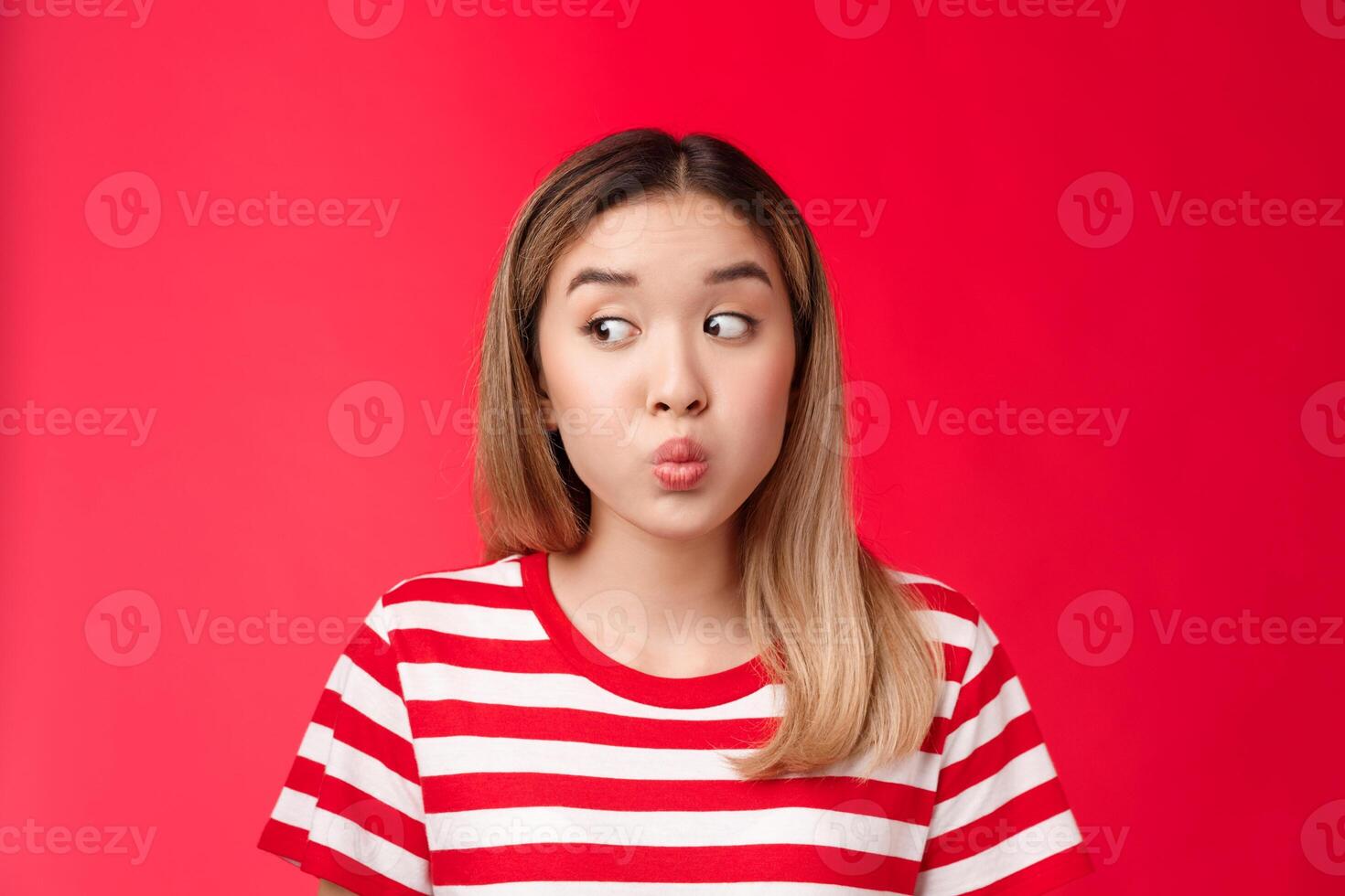 Close-up silly tender young modern asian girl blond haircut hold breath, folding lips and pouting look away as if hiding secretn, stand red background innocent clueless seal lips with promise photo
