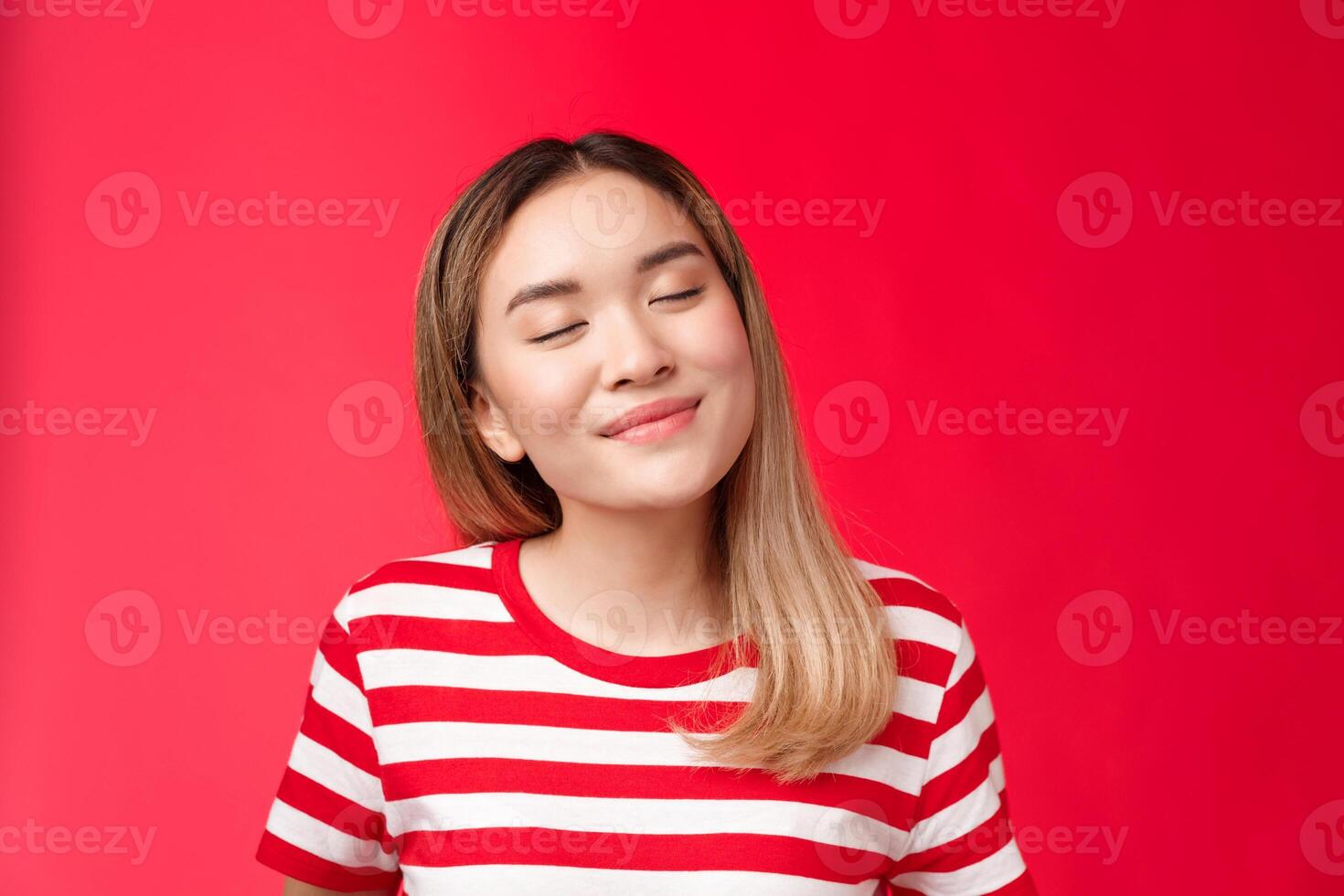 Close-up romantic tender happy asian woman tilt head close eyes joyfully smiling recalling nice lovely moment, daydreaming delicious coffee with dessert, stand red background relaxed cheerful photo