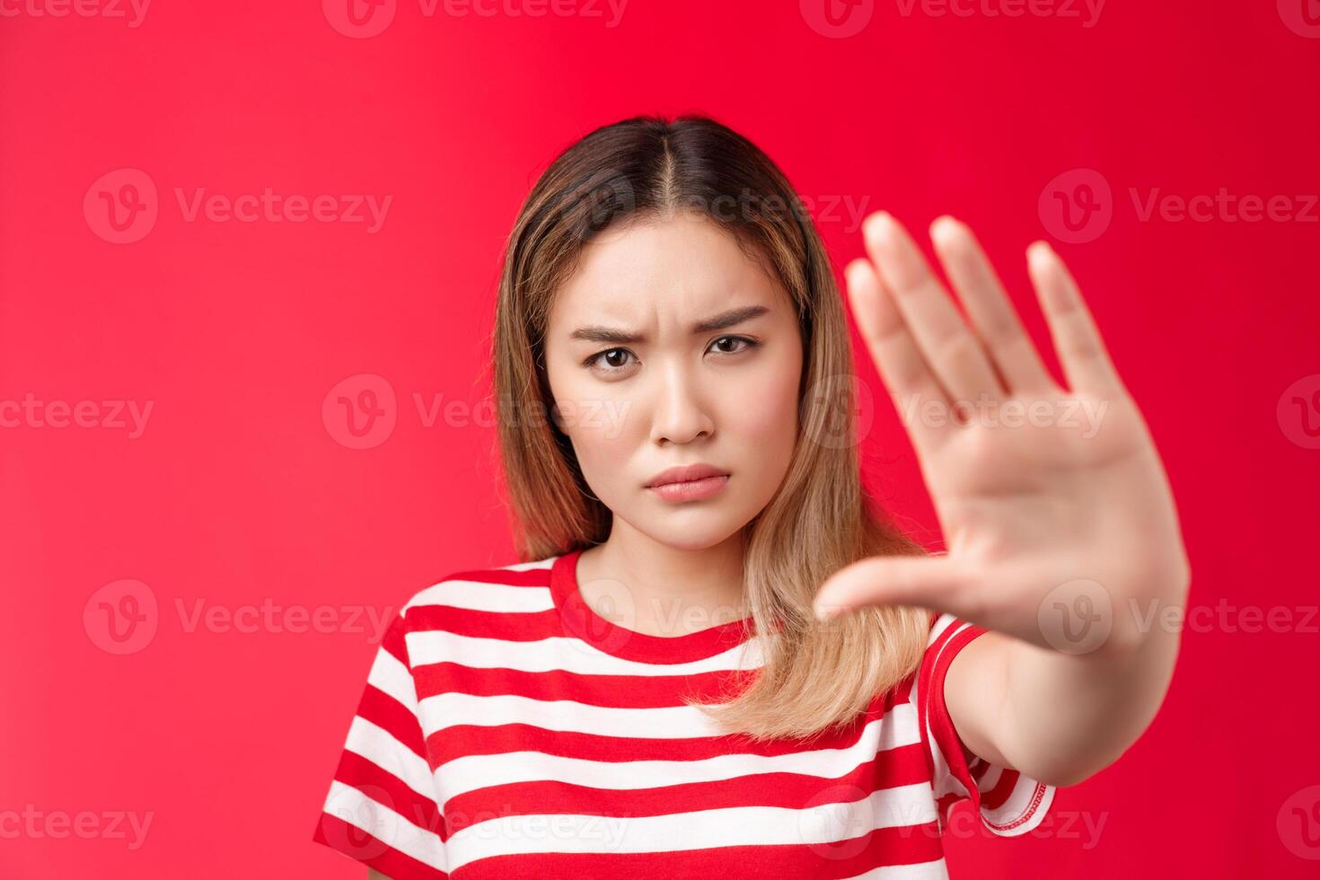 Serious-looking alarmed angry asian woman pull hand forward stop, no sign, demanding and prohibiting behave rude, stand red background intense rejecting awful offer, stand red background photo