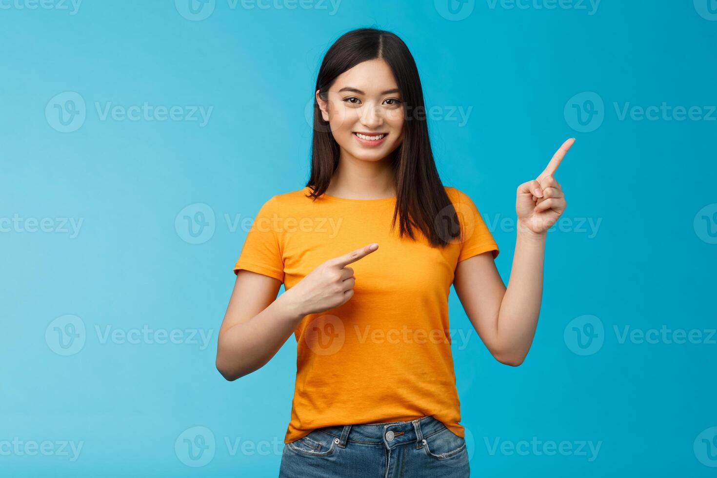 Friendly cheerful asian brunette girl inviting visit link interesting place, pointing upper right corner smiling joyfully camera, telling you about good promotion, stand blue background upbeat photo