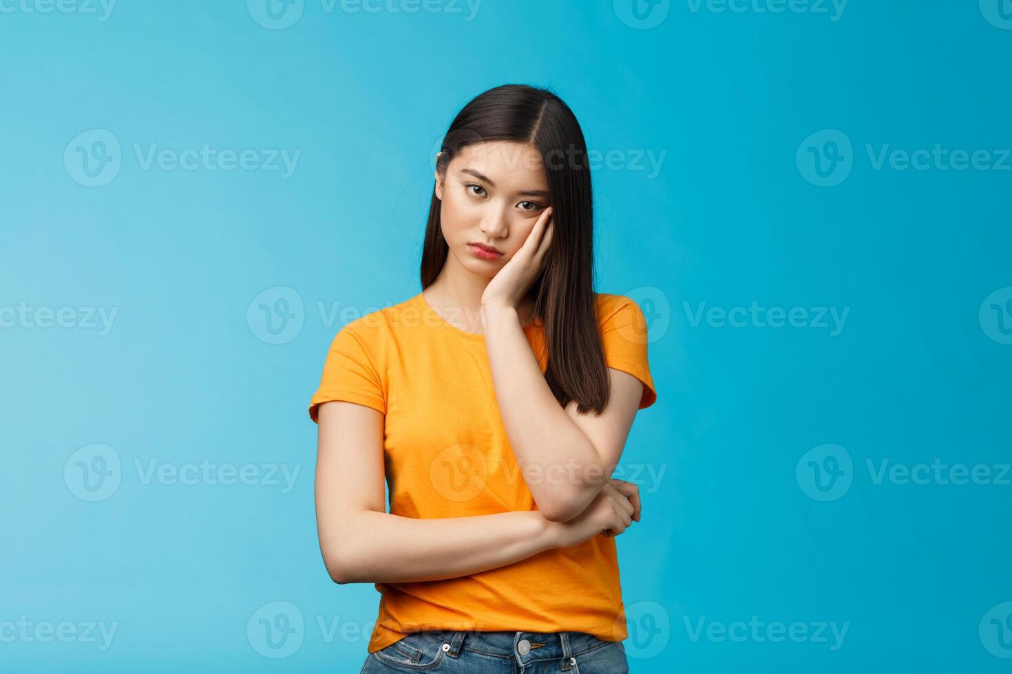 Sad bored asian female student attend boring uninteresting lecture lean face palm, look indifferent express apathy dislike, grimacing and sulking disappointed stand blue background bothered photo