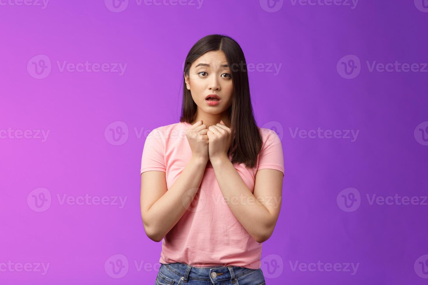 Timid concerned cute asian girl express empathy and worry, press hands heart upset, sorry for friend, open mouth, sighing sad nervous, hesitating, anxiously saying love you, stand purple background photo