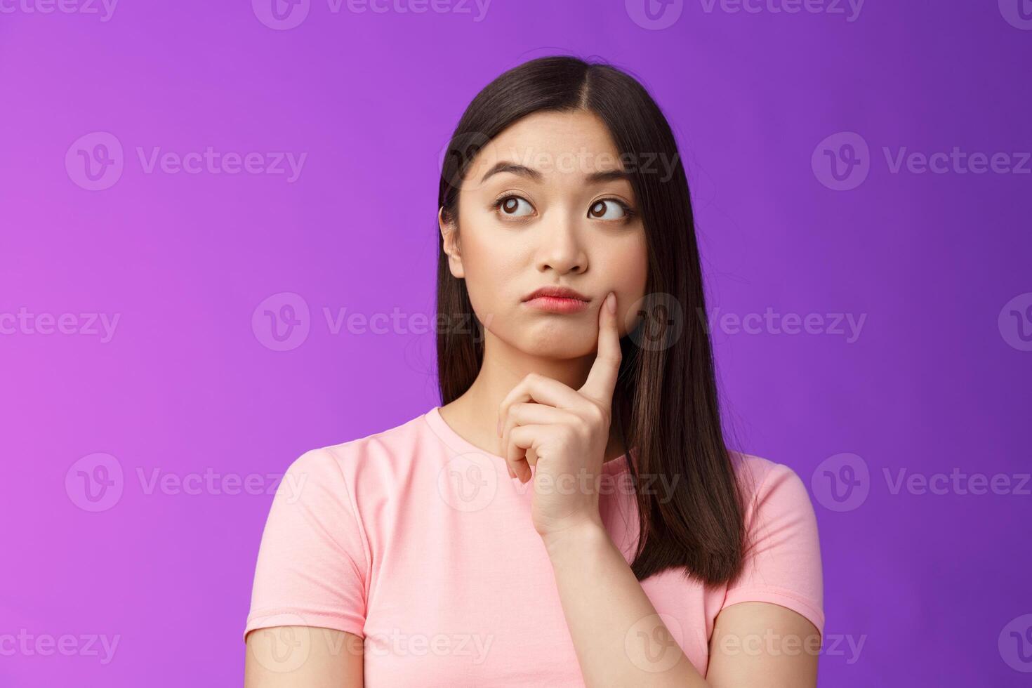 Close-up thoughtful cute asian girl dreamy standing purple background, touch cheek, turn left, thinking, doubting how act, wondering information, contemplating view from window photo