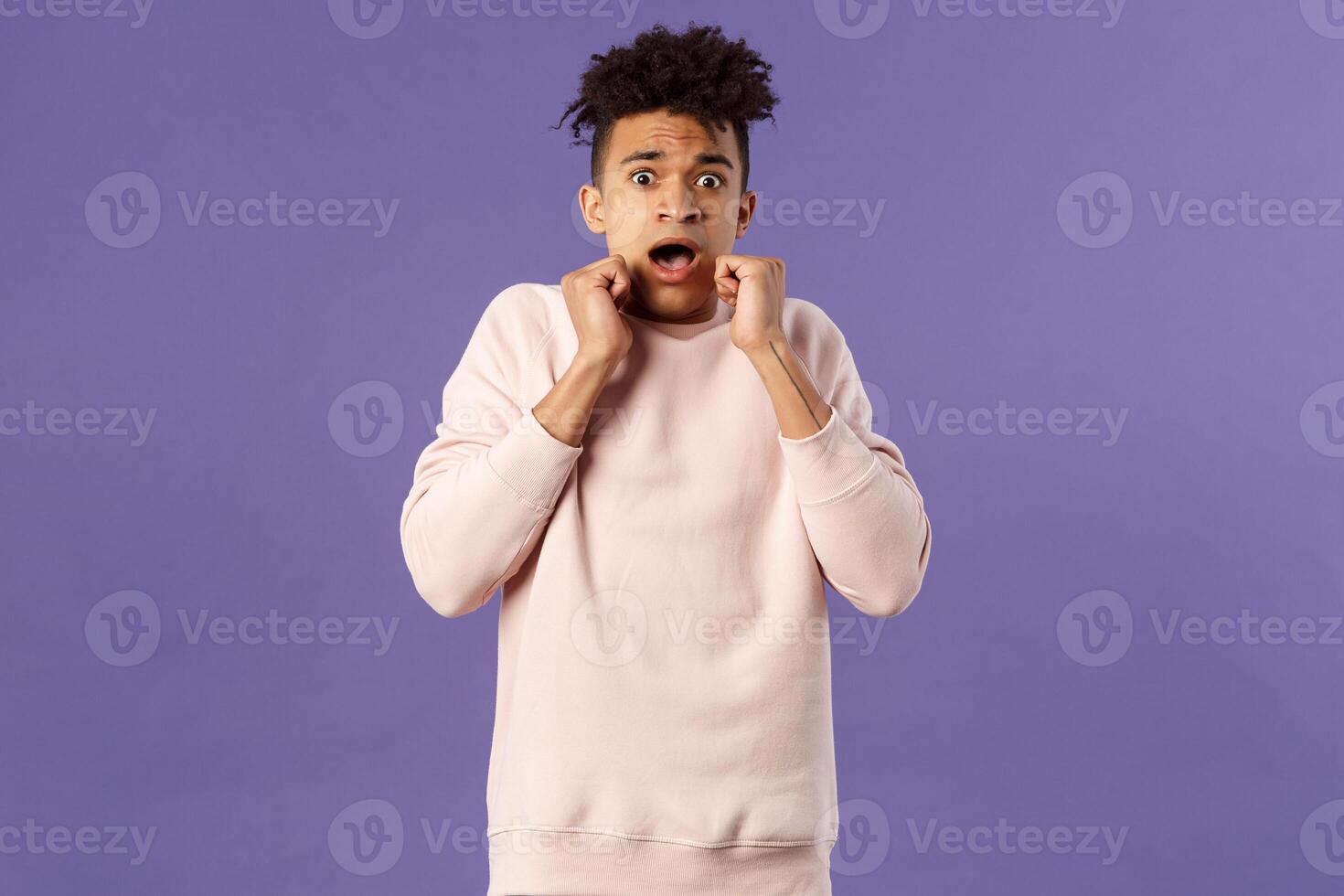 Portrait of scared hispanic guy screaming from fright, hold hands near face, open mouth gasping express fear and terrified emotion from watching horror movie, terrible accident, purple background photo