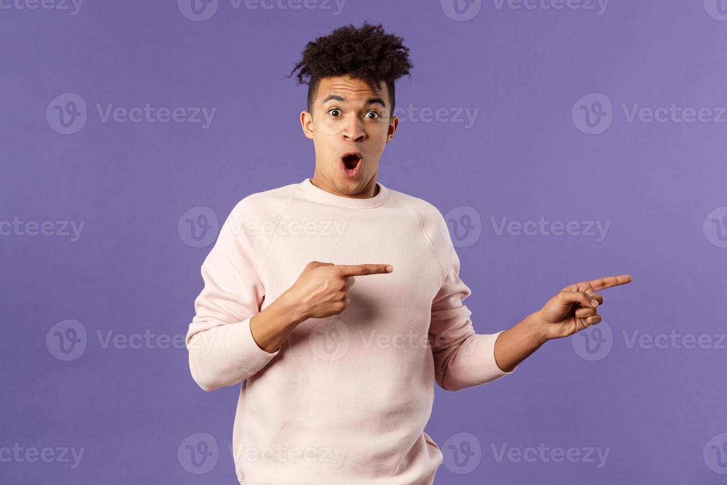 Portrait of excited, handsome young hispanic man talking about amazing party going nearby, describe incredible deal, open mouth wondered, pointing fingers right, recommend buy or download photo