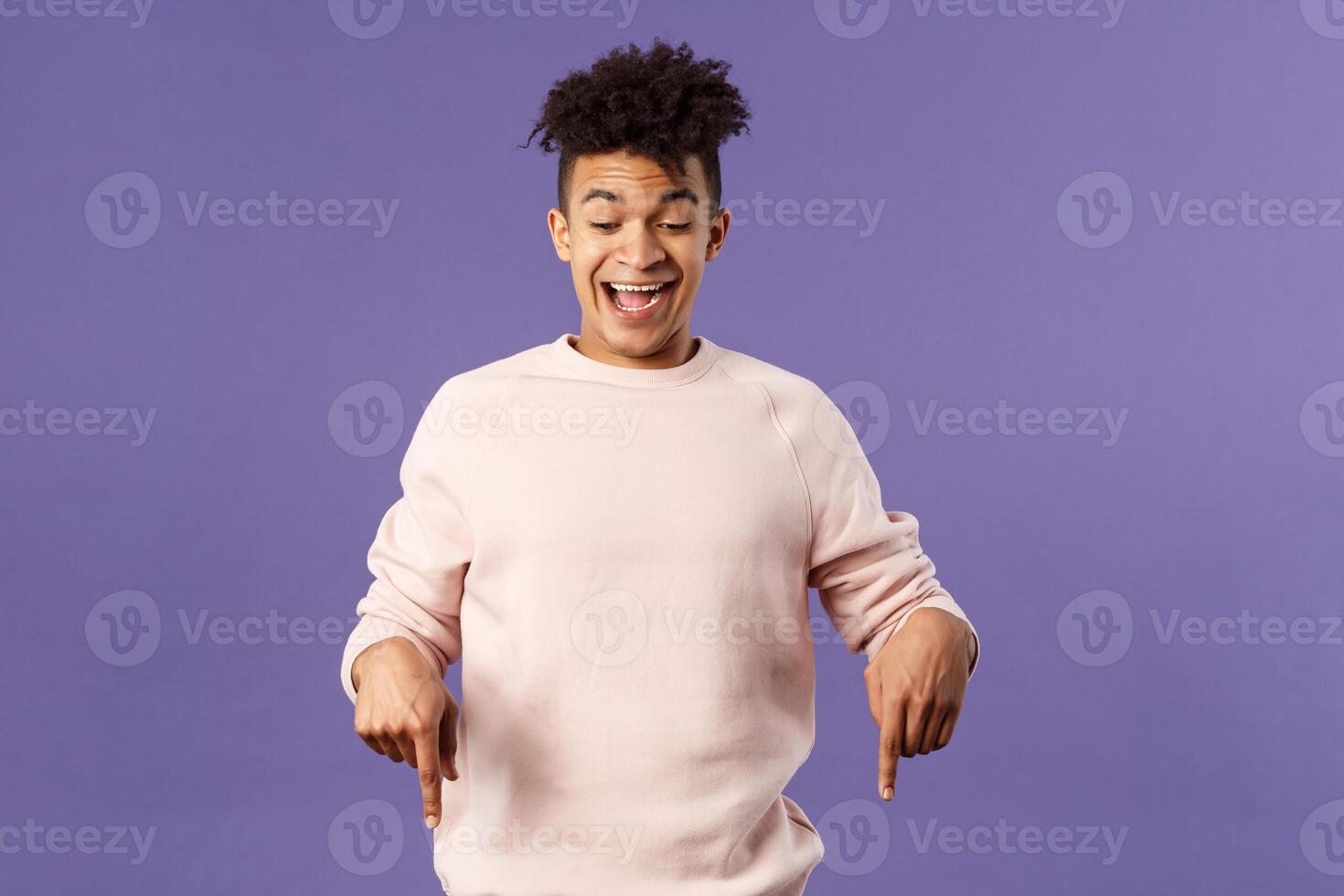 Joyful good-looking hipster guy with dreads rejoicing over good news, best deal ever in online store, favorite game finally in stock, pointing fingers down and rejoicing, purple background photo