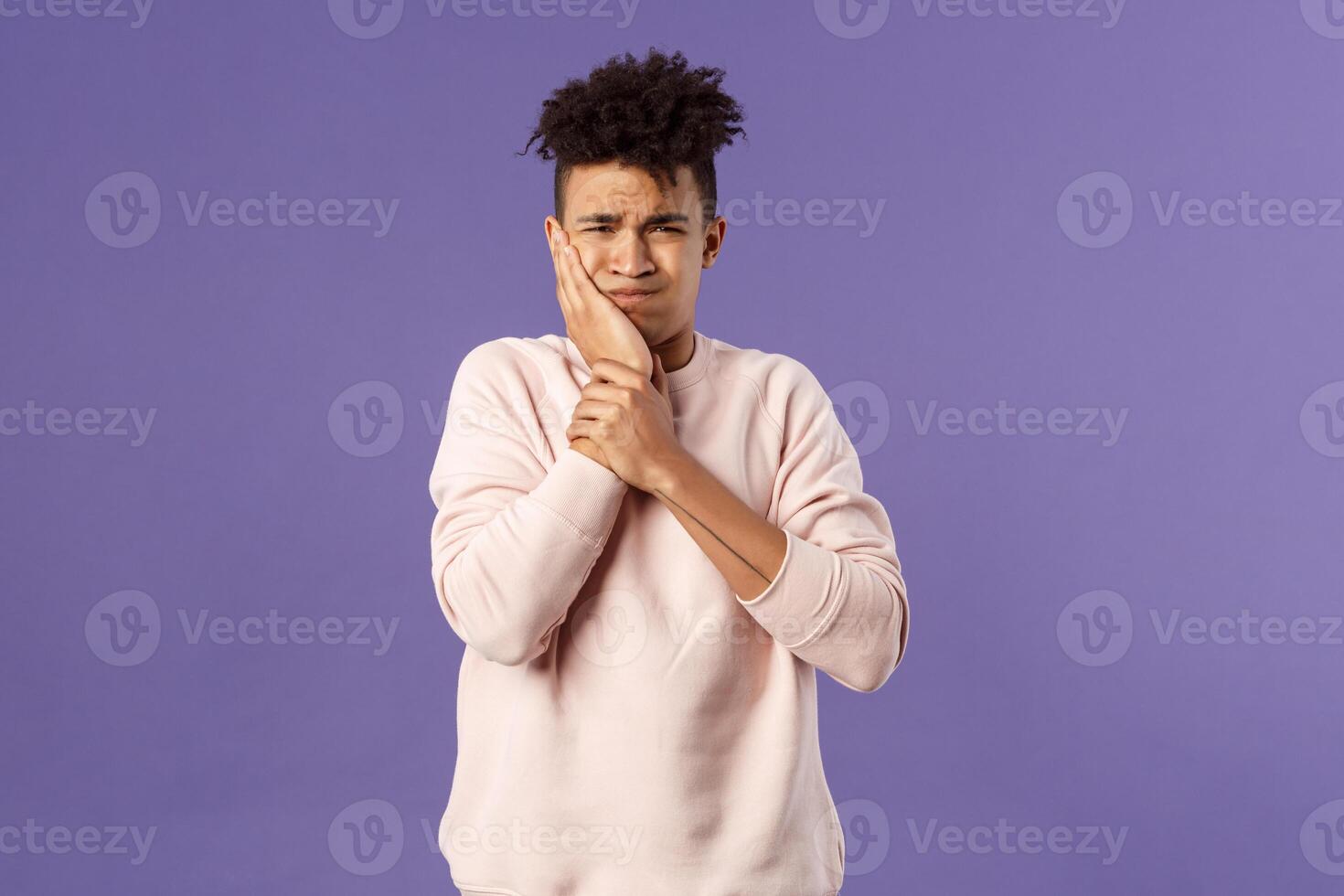 Portrait of troubled young man feeling painful ache in tooth, have toothache or decay, touching swallen cheek grimacing uneasy, need see dentist, waiting in line for appointment, purple background photo